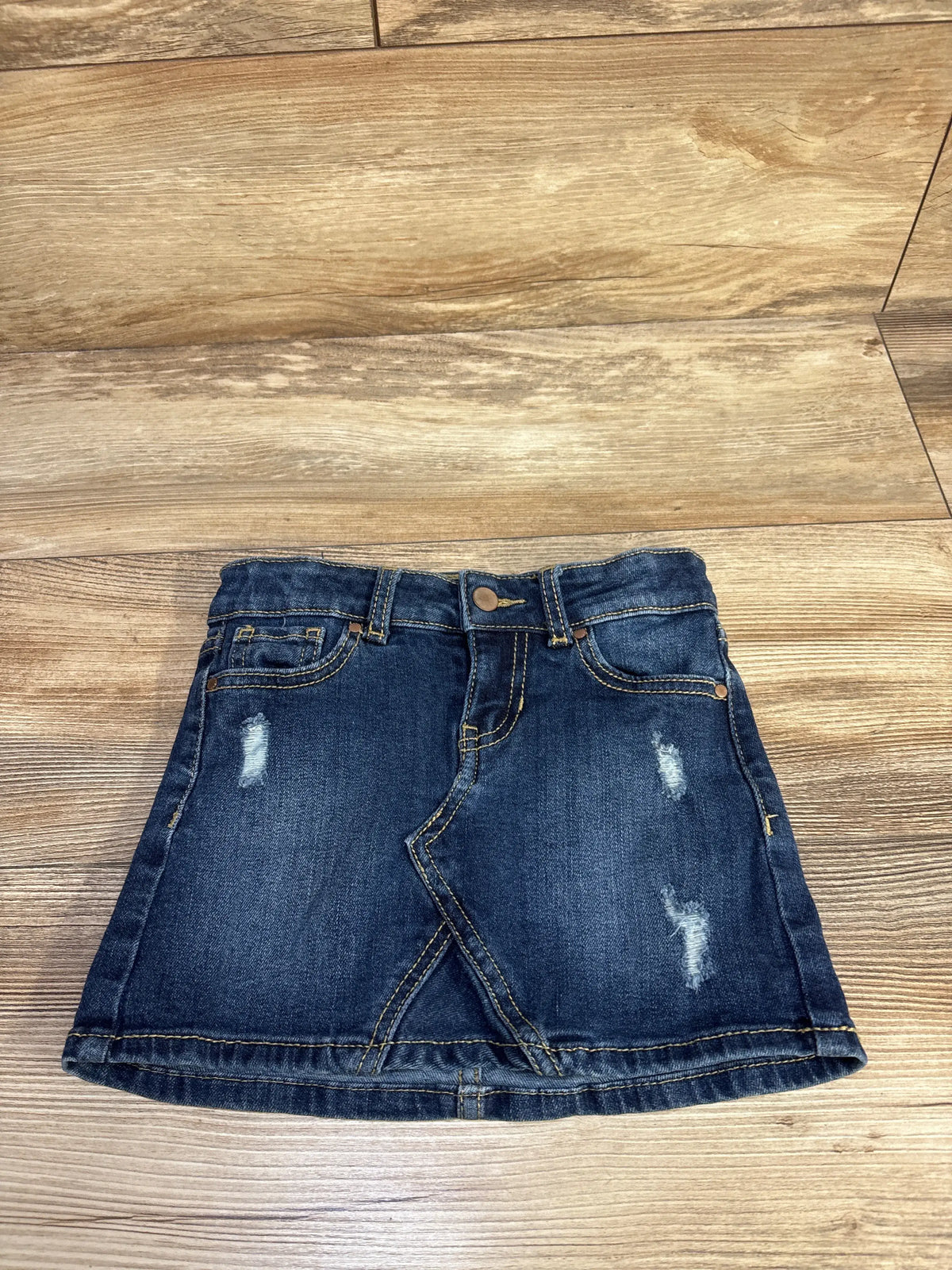Front view of Wonder Nation blue denim skirt showcasing distressed details, pockets, and belt loops on a wood floor
