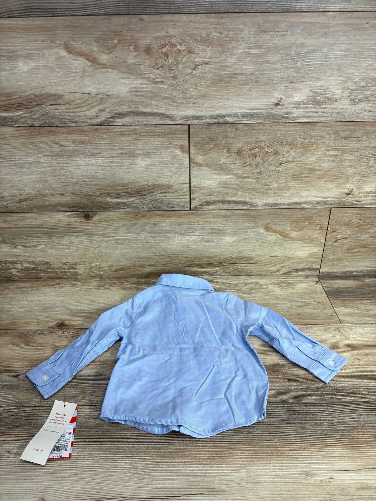 Light blue long sleeve button-up toddler shirt with tag on wood background