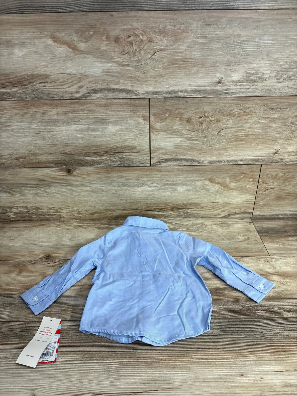 Light blue long sleeve button-up toddler shirt with tag on wood background