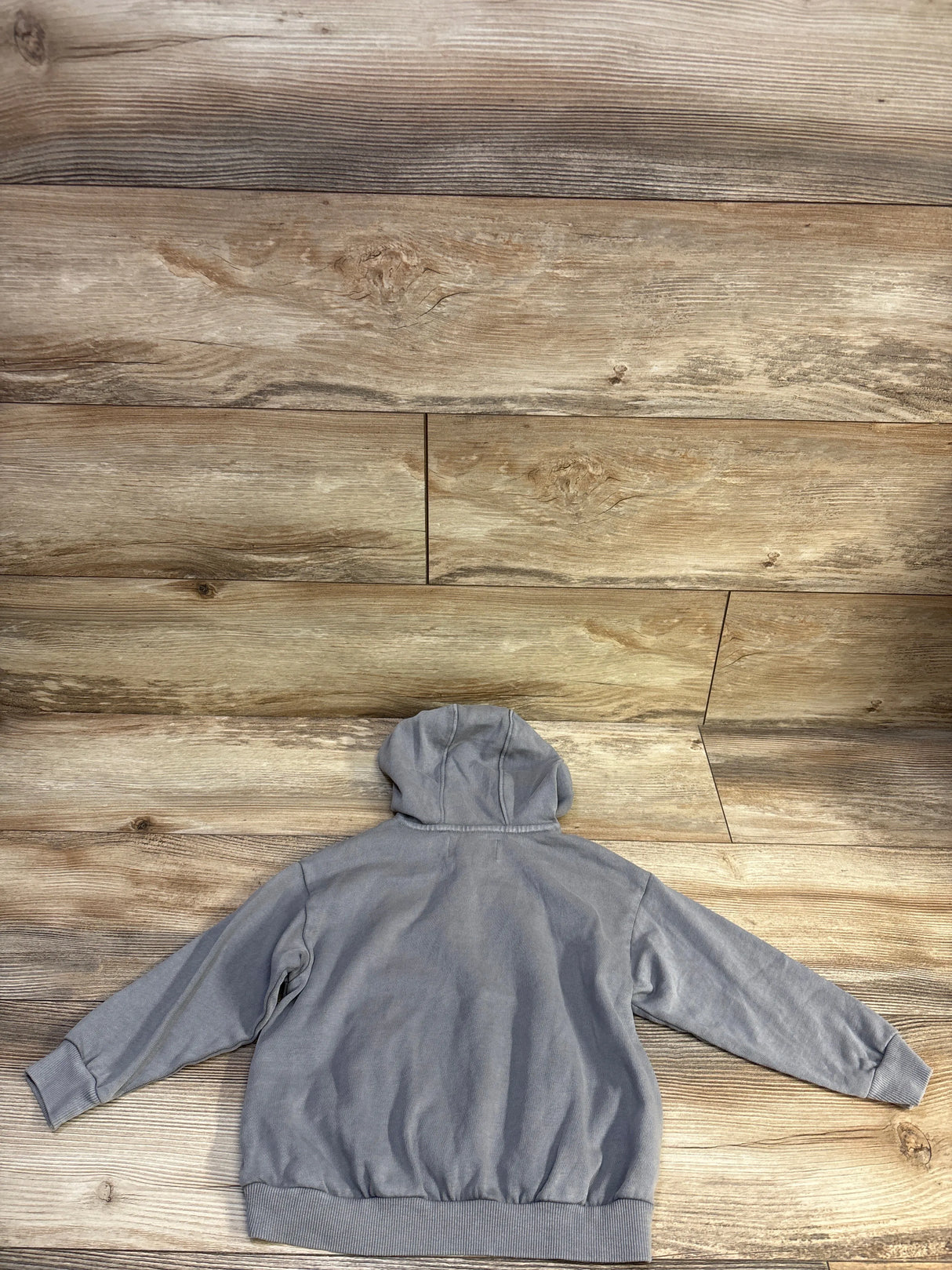 Back view of Old Navy Henley pullover hooded sweatshirt in grey showing hood, long sleeves, and ribbed cuffs on wood background