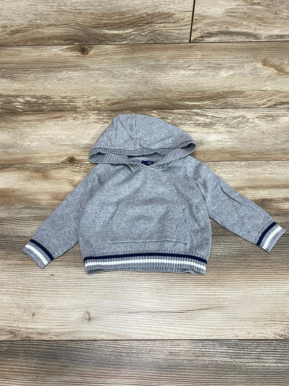 Front view of Janie & Jack grey hooded baby sweater (6–12M) showcasing kangaroo pocket and navy-white striped cuffs and hem on wood background