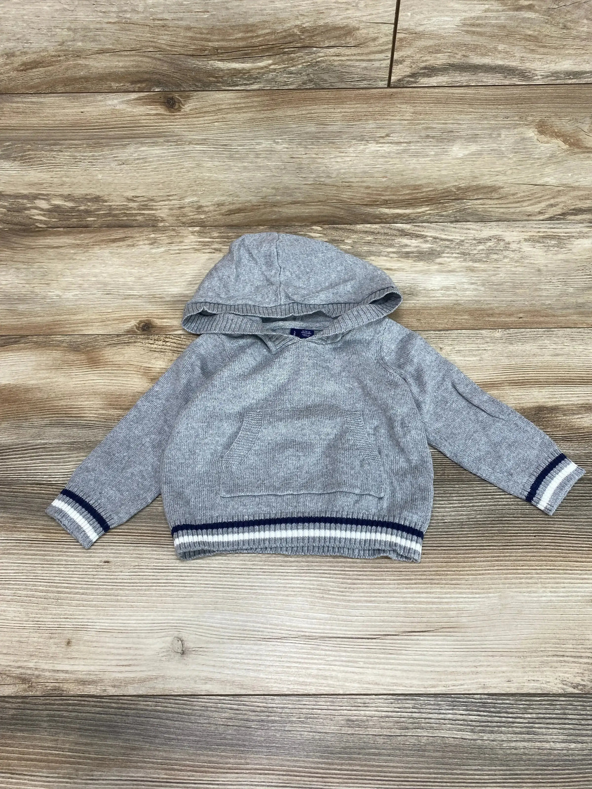 Front view of Janie & Jack grey hooded baby sweater (6–12M) showcasing kangaroo pocket and navy-white striped cuffs and hem on wood background