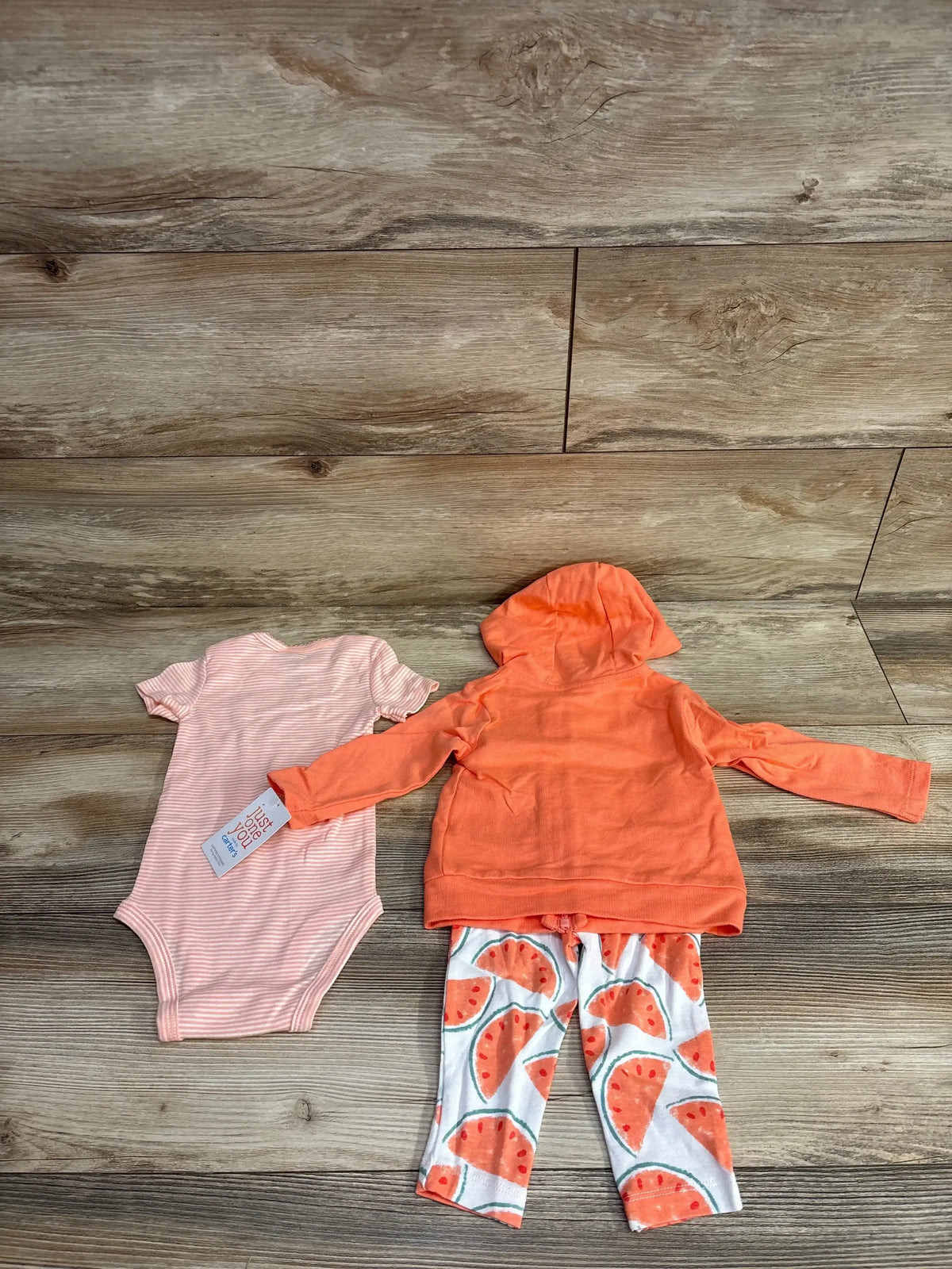Infant pink striped onesie and orange hooded jacket with watermelon print leggings on wooden floor