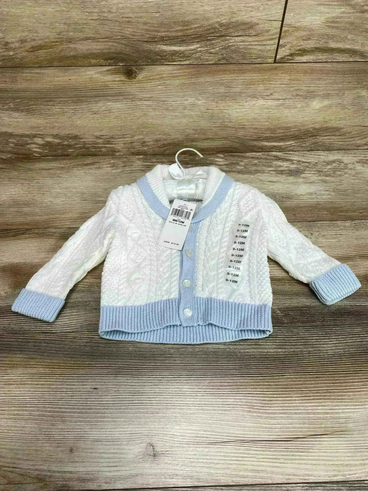 Front view of baby Ralph Lauren white cable-knit shawl-collar cardigan showcasing light blue trim and buttons on a hanger over wood background, size 9-12M