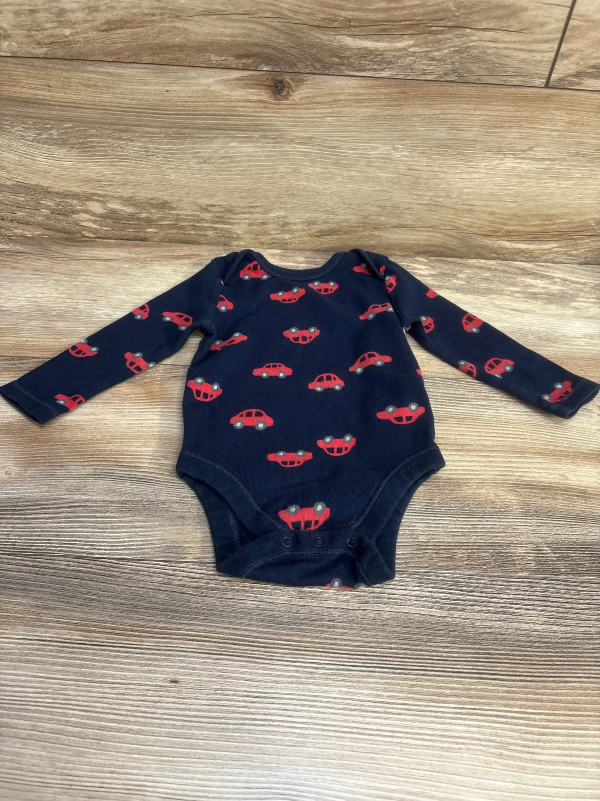 Flat-lay of navy Old Navy long-sleeve car-print baby bodysuit showing red car pattern on wood background