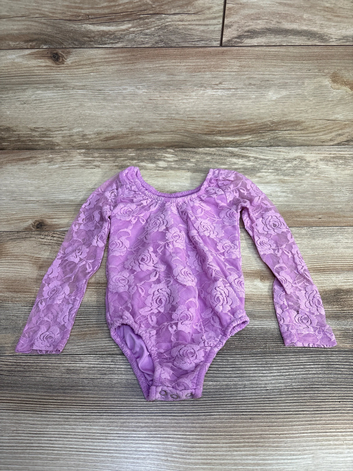 Pink lace long sleeve baby bodysuit with snap closure on wood background