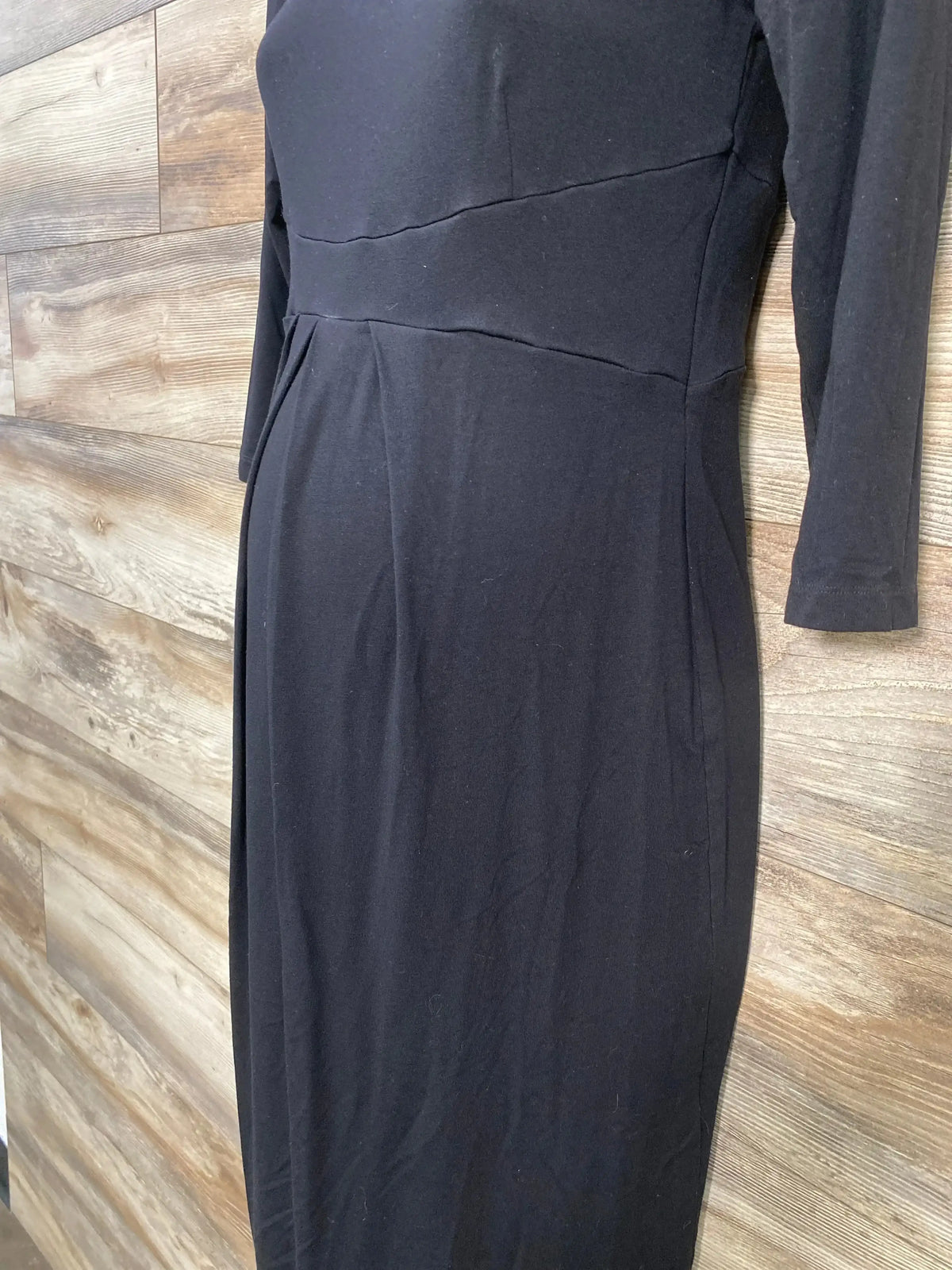 Close up front view of Isabella Oliver black maternity dress with empire waist seam and long sleeves on wood plank floor