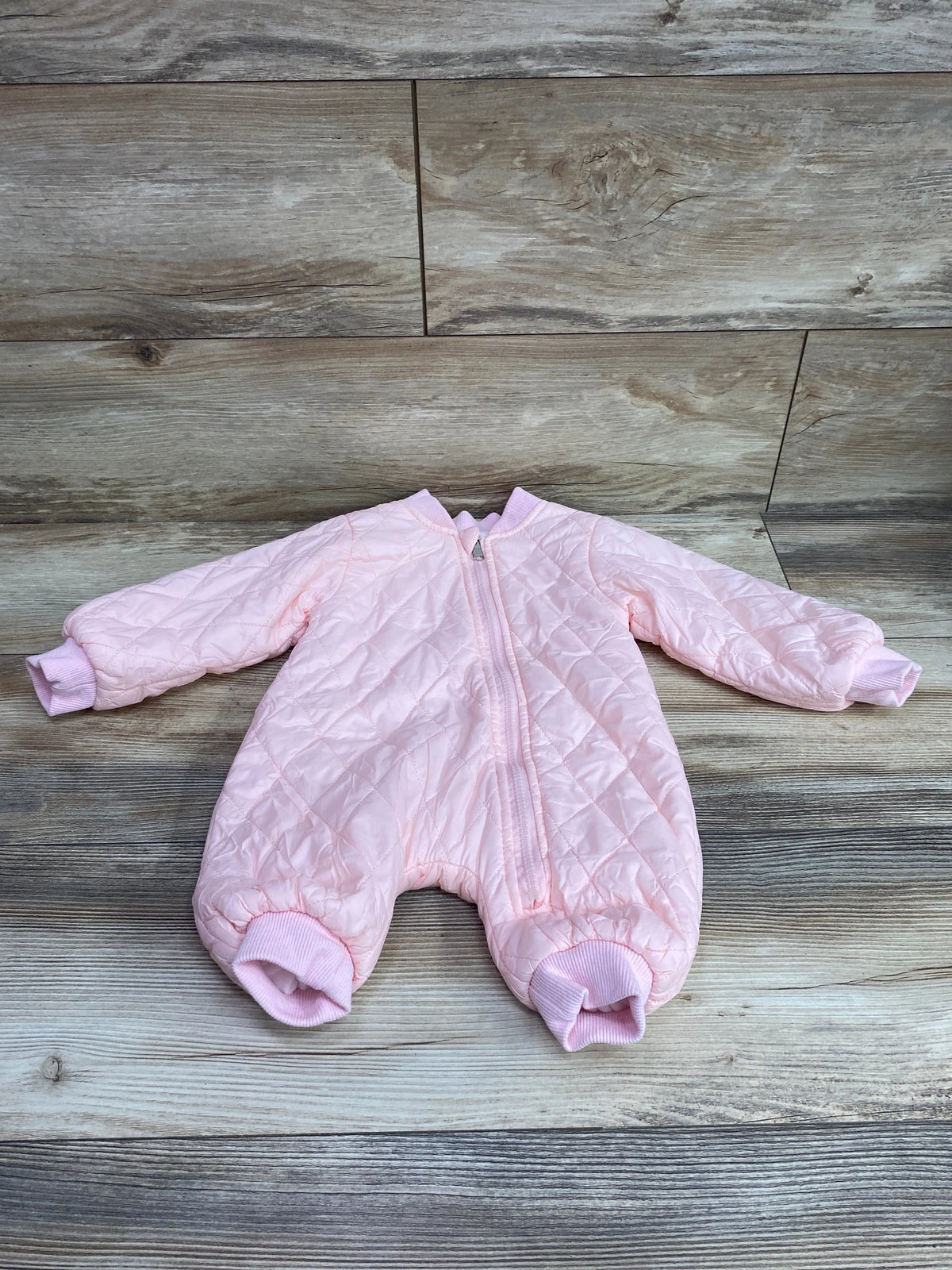 Pink quilted baby coveralls size 3m with zipper closure on a wood-grain background
