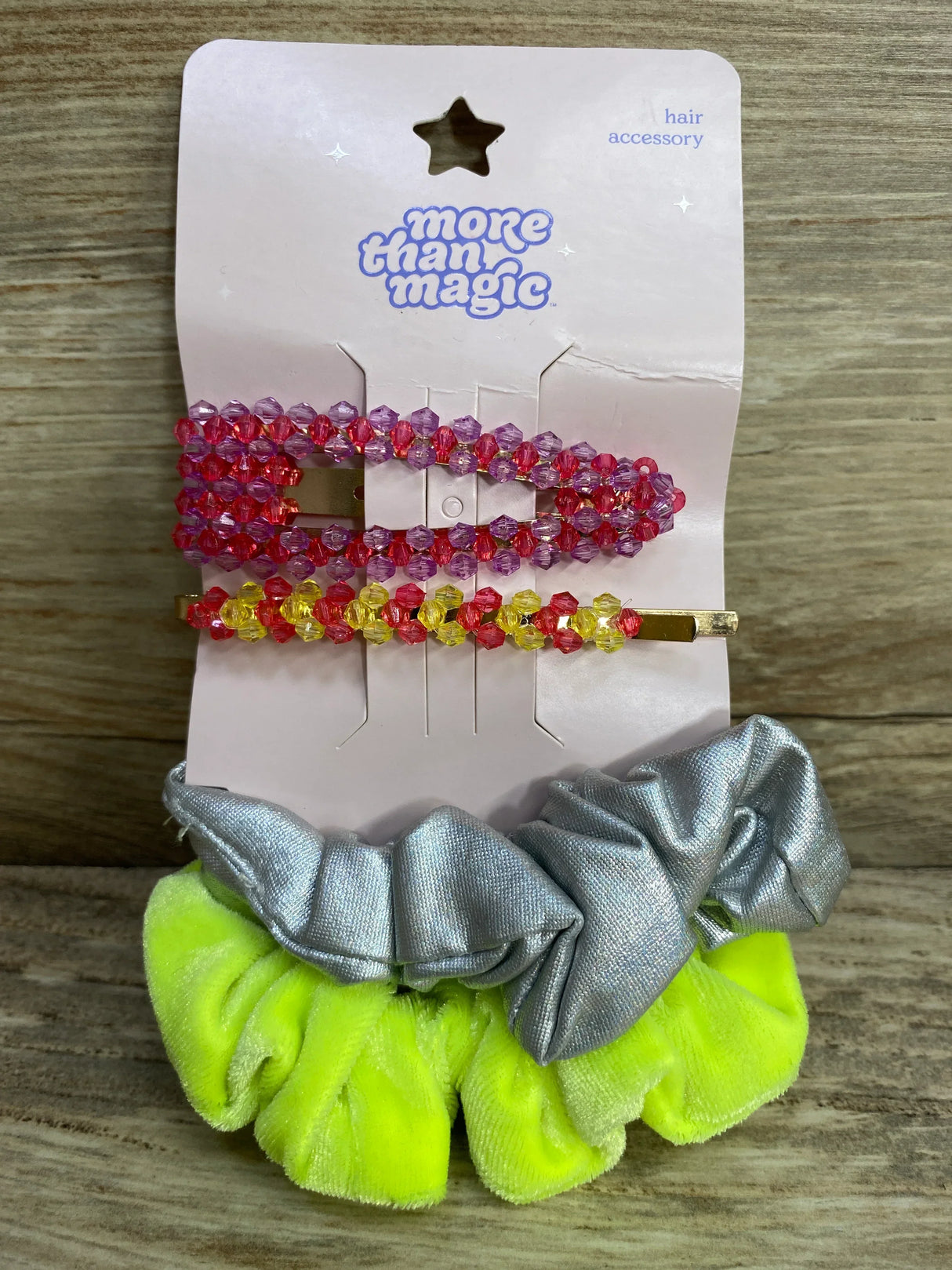 More Than Magic hair accessory set with pink and yellow beaded clips and neon green and silver scrunchies on wood surface