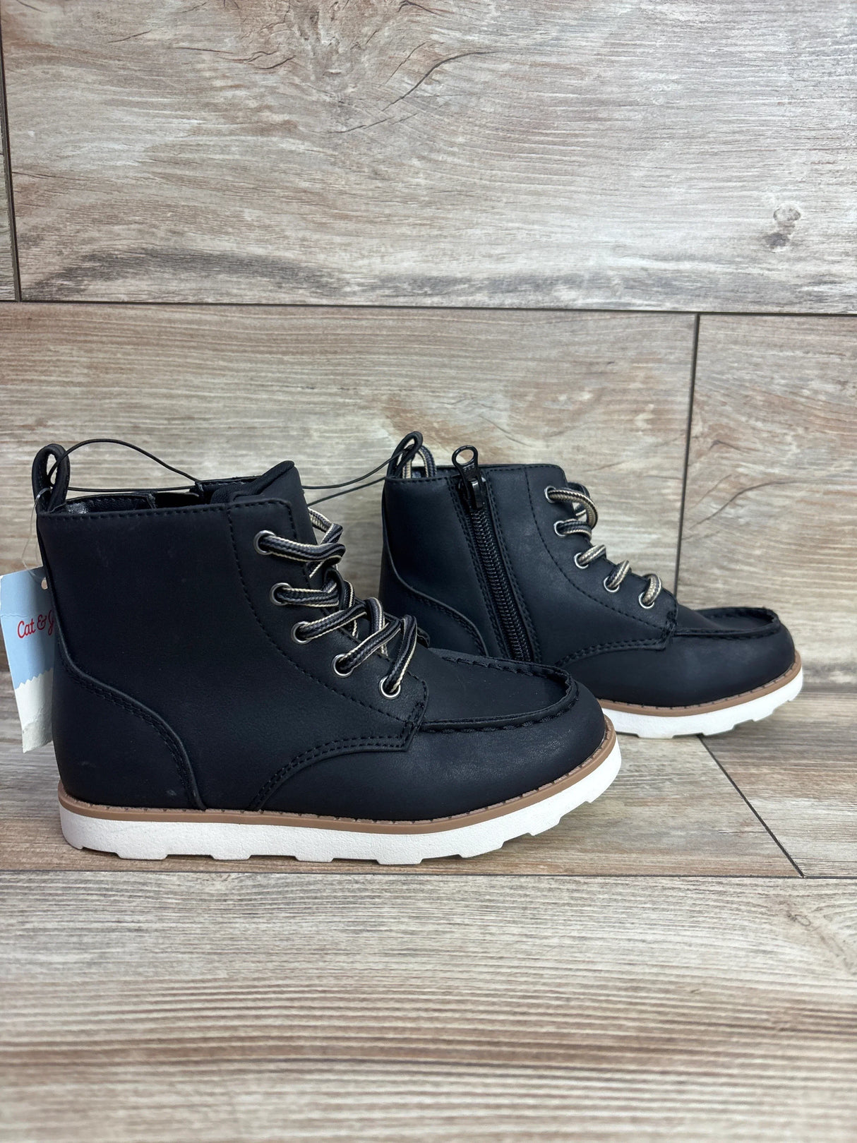 Side view of Cat & Jack Greyson toddler boots size 11C showing black lace-up upper, side zipper, moc-toe stitching and white soles on wood background