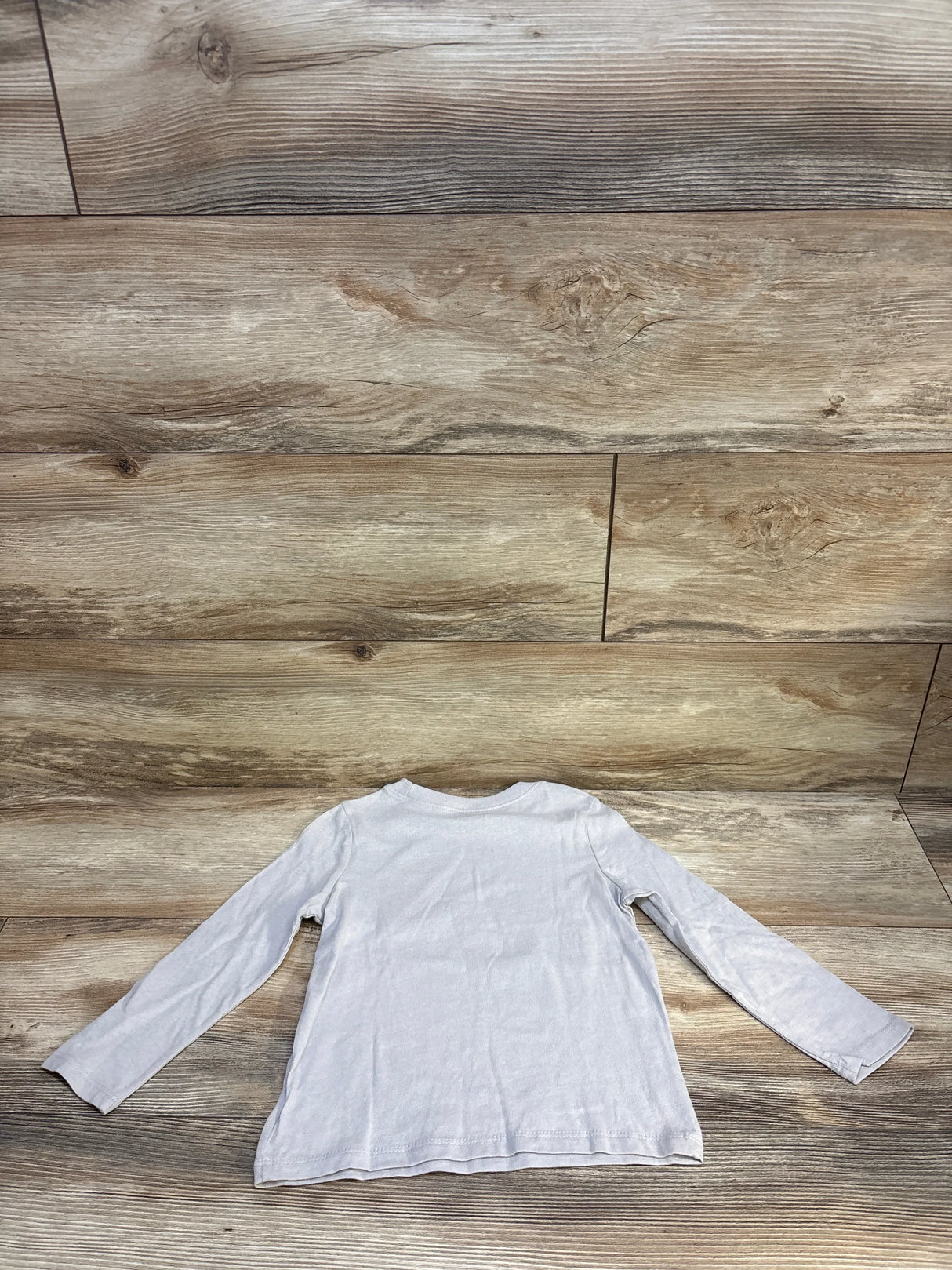 Back view of a plain long sleeve white kids shirt on wood background