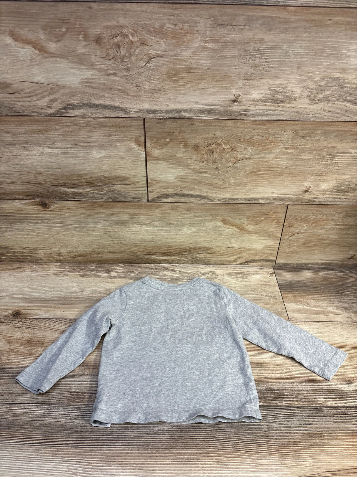 Back view of grey Baby Gap long-sleeve toddler shirt showing scalloped hem on wood floor background