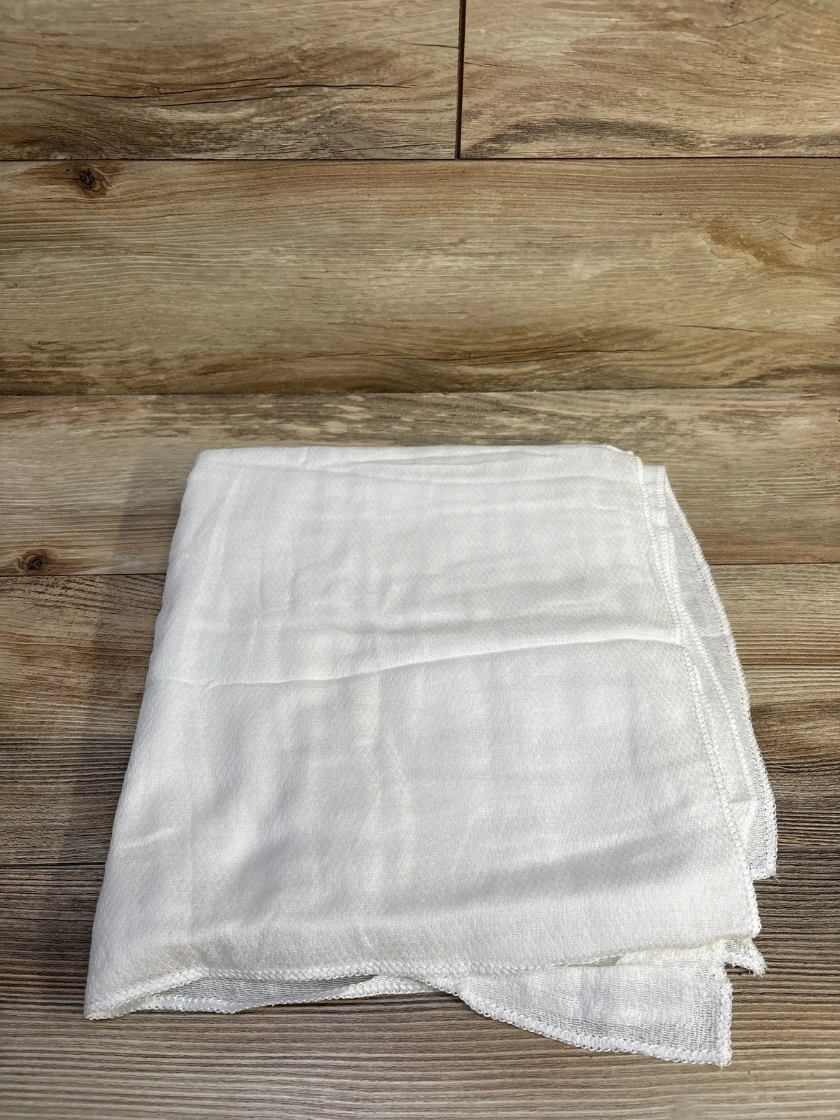 Top-down view of folded white receiving blankets (5-pack) showcasing lightweight muslin texture on wood floor background