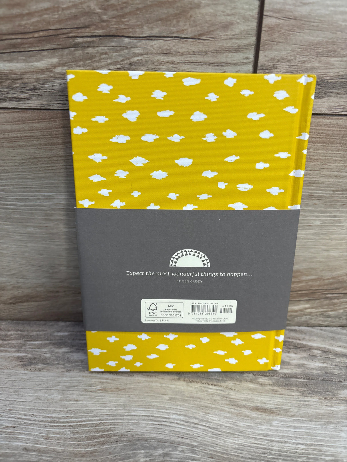 Yellow hardcover notebook with white cloud pattern on wood surface, gray band with quote