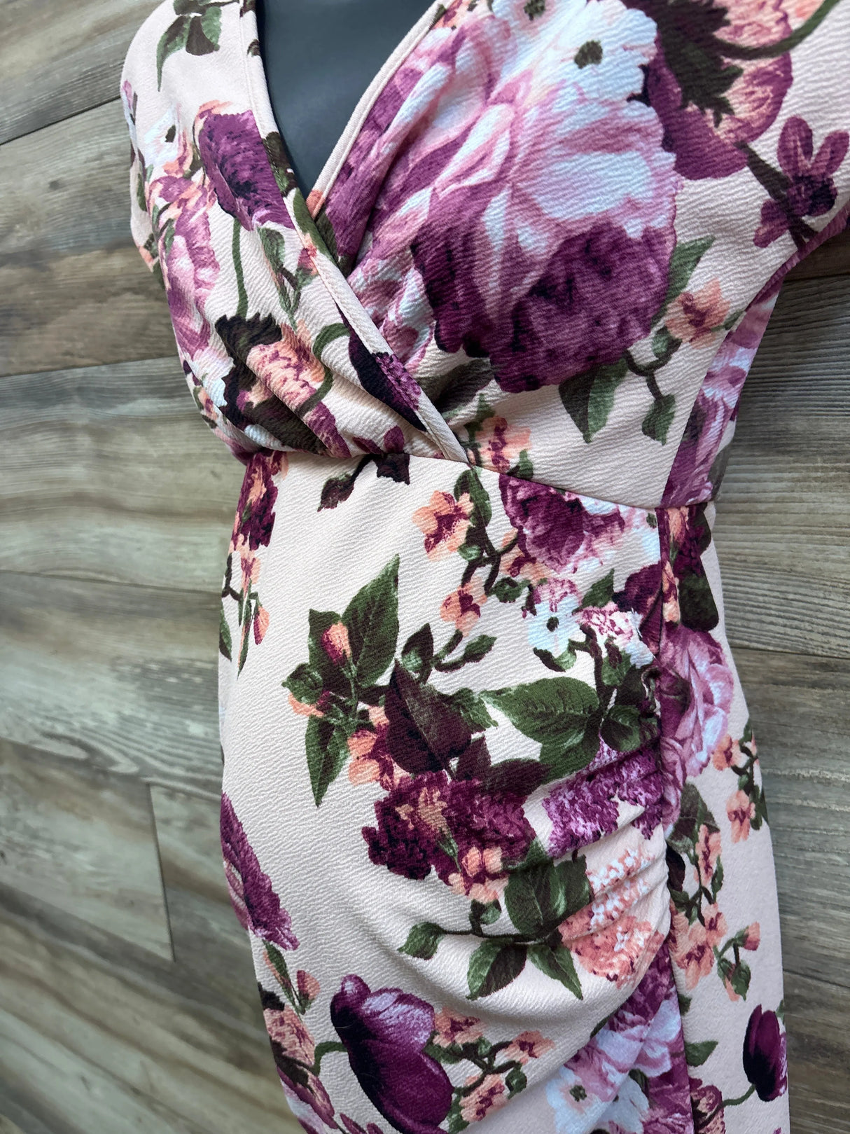Close-up side view of Pinkblush rose floral maternity wrap dress showing V-neck bodice and side ruching, wood background