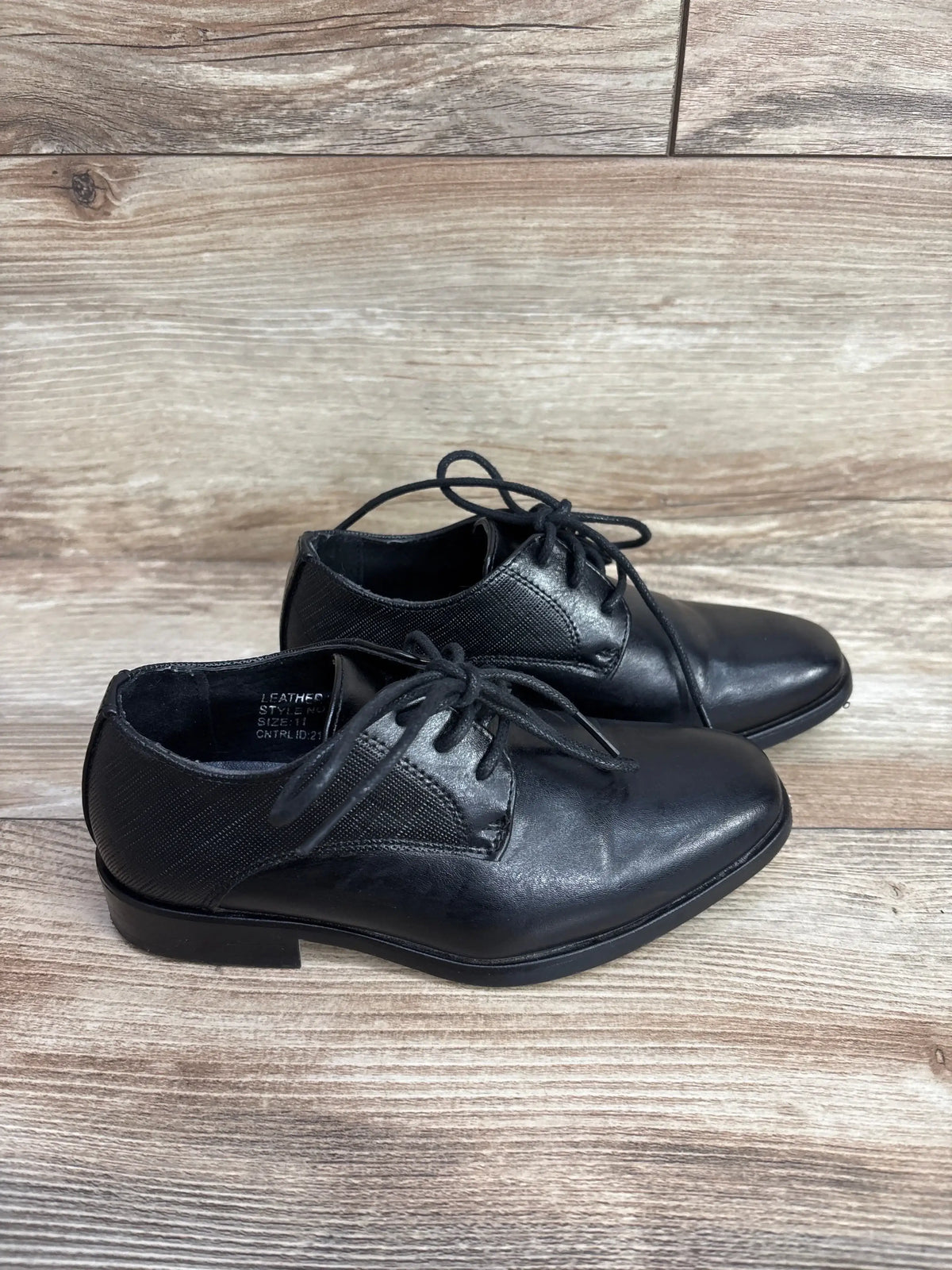 Three-quarter view of Bonafini Kids K-154 black leather dress shoes, lace-up with stitched toe, on wooden floor