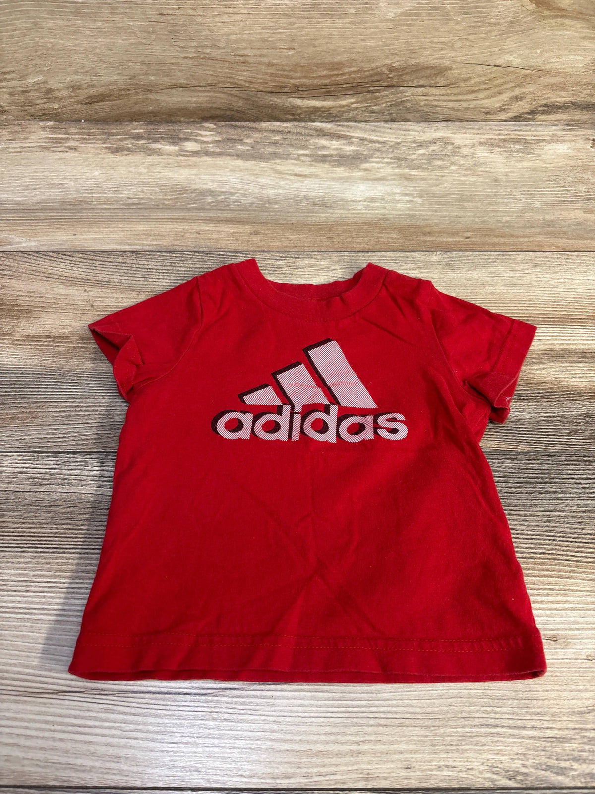 Red Adidas infant t-shirt size 3m featuring the brand logo, laid flat on a wood-grain surface.