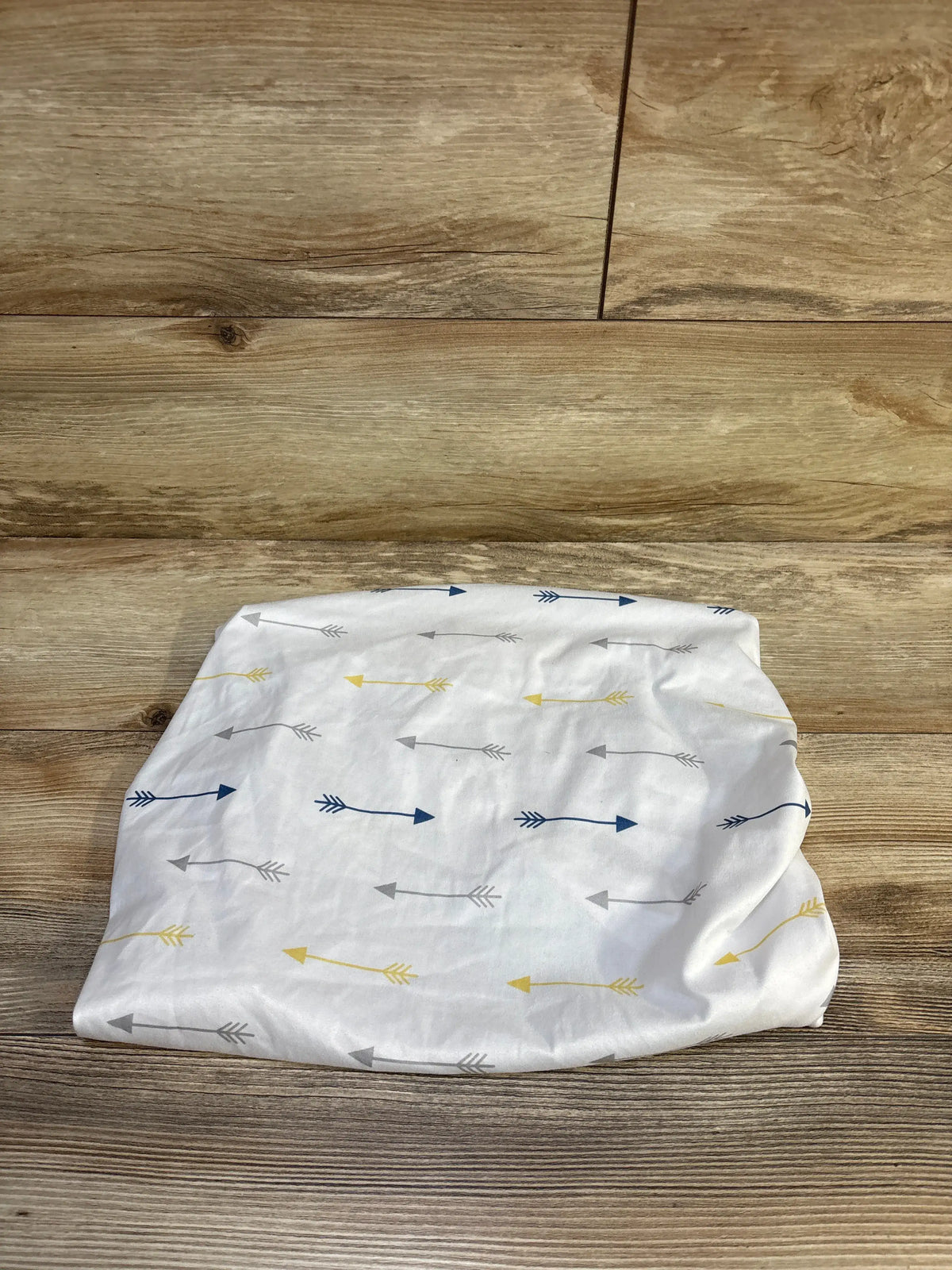 Top-down view of fitted bassinet sheet 20x35 showing navy, gray, and yellow arrows on white fabric on wood background