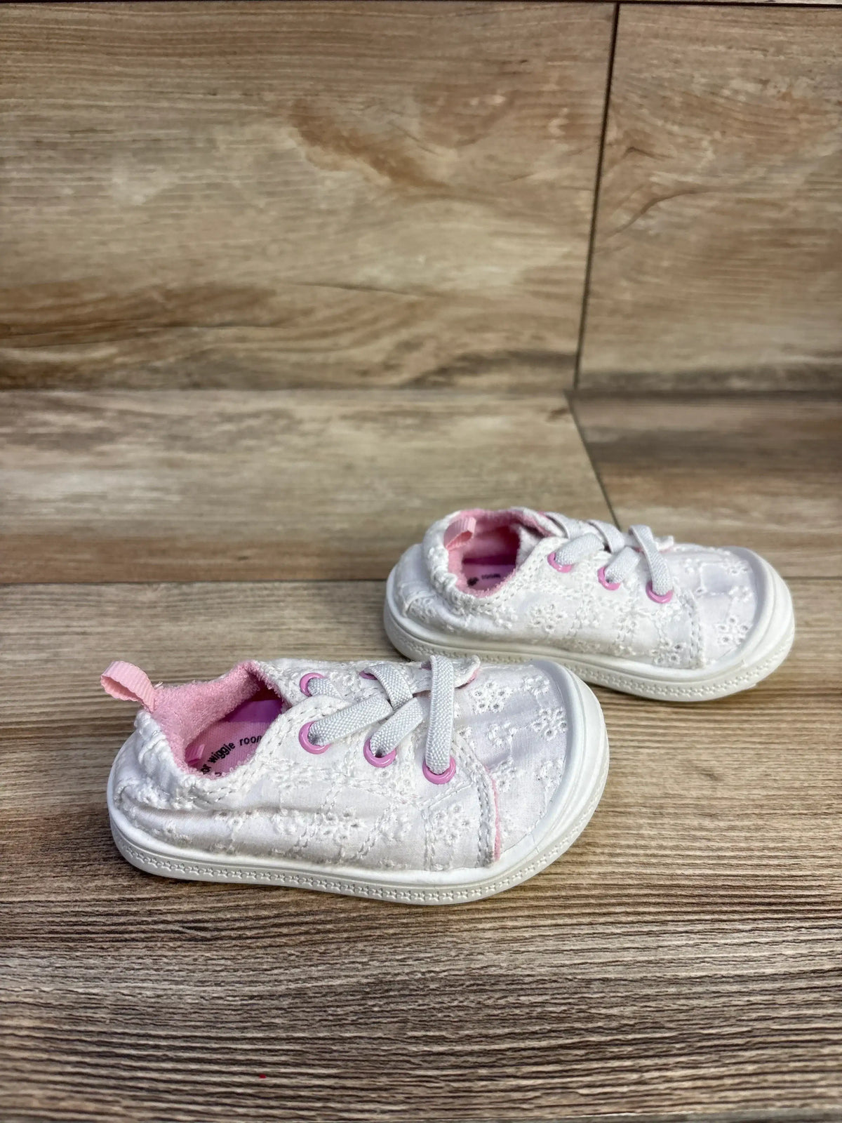 Three-quarter view of white baby Wonder Nation eyelet sneakers with pink eyelets and lining, elastic laces, rubber toe on light wood floor