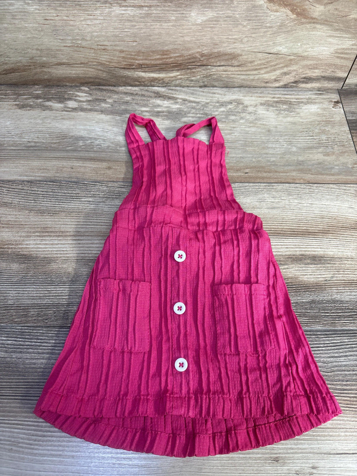 Flat-lay pink toddler skirtall (12-18 months) showing crinkled texture, three white buttons and two front pockets on wood background