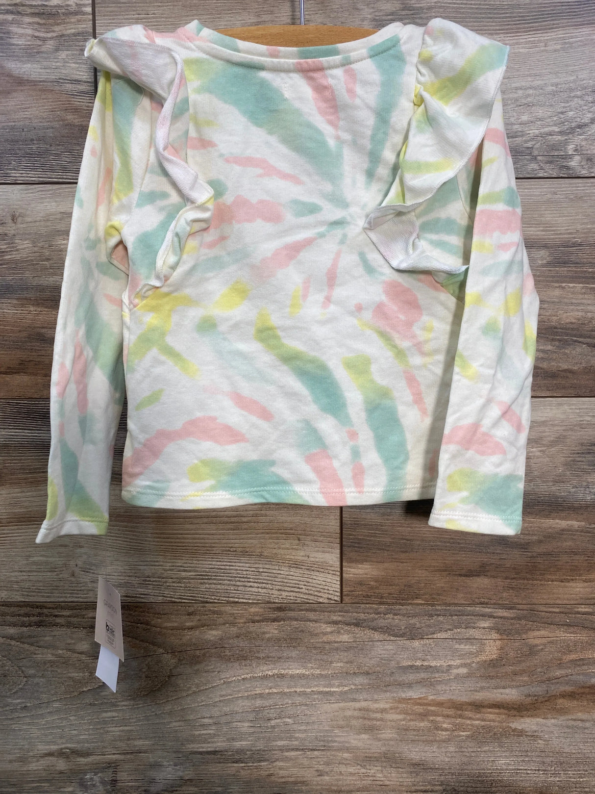 Pastel tie-dye long sleeve toddler shirt with ruffled shoulders on wooden surface