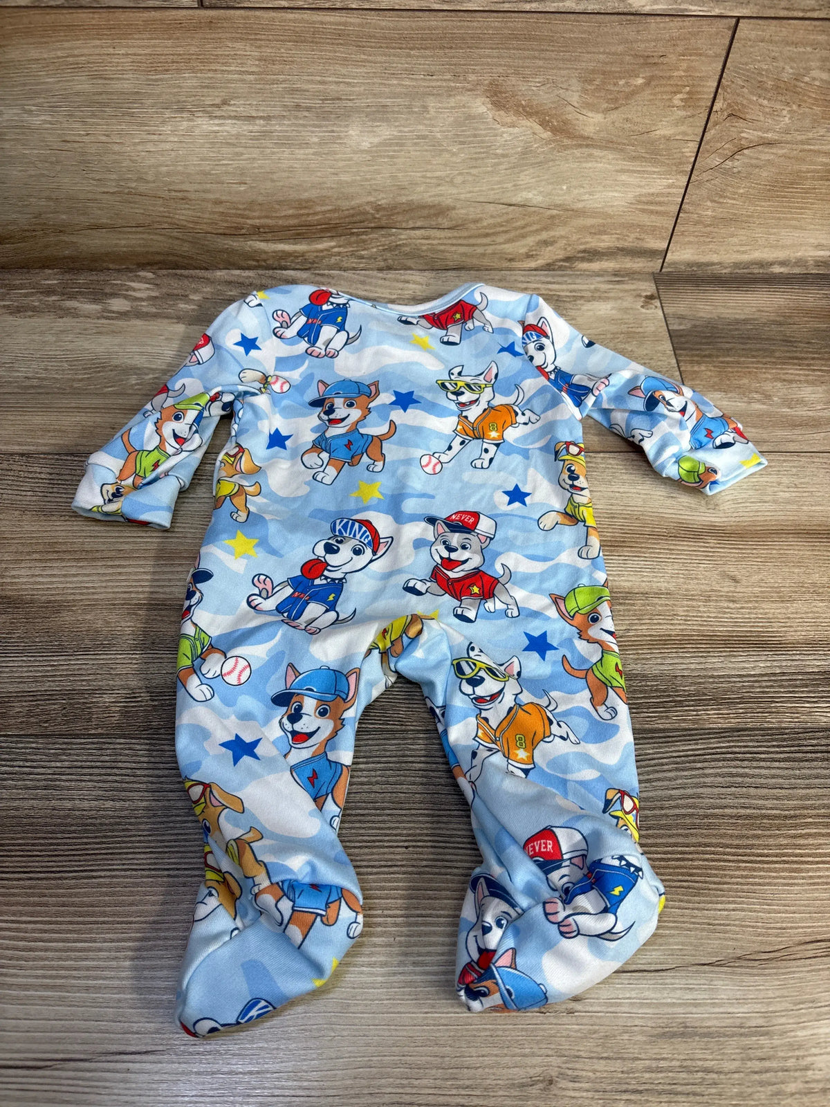 Top-down view of Shein x PAW Patrol blue sleeper showcasing its all-over character print and footed design on a wood-grain background