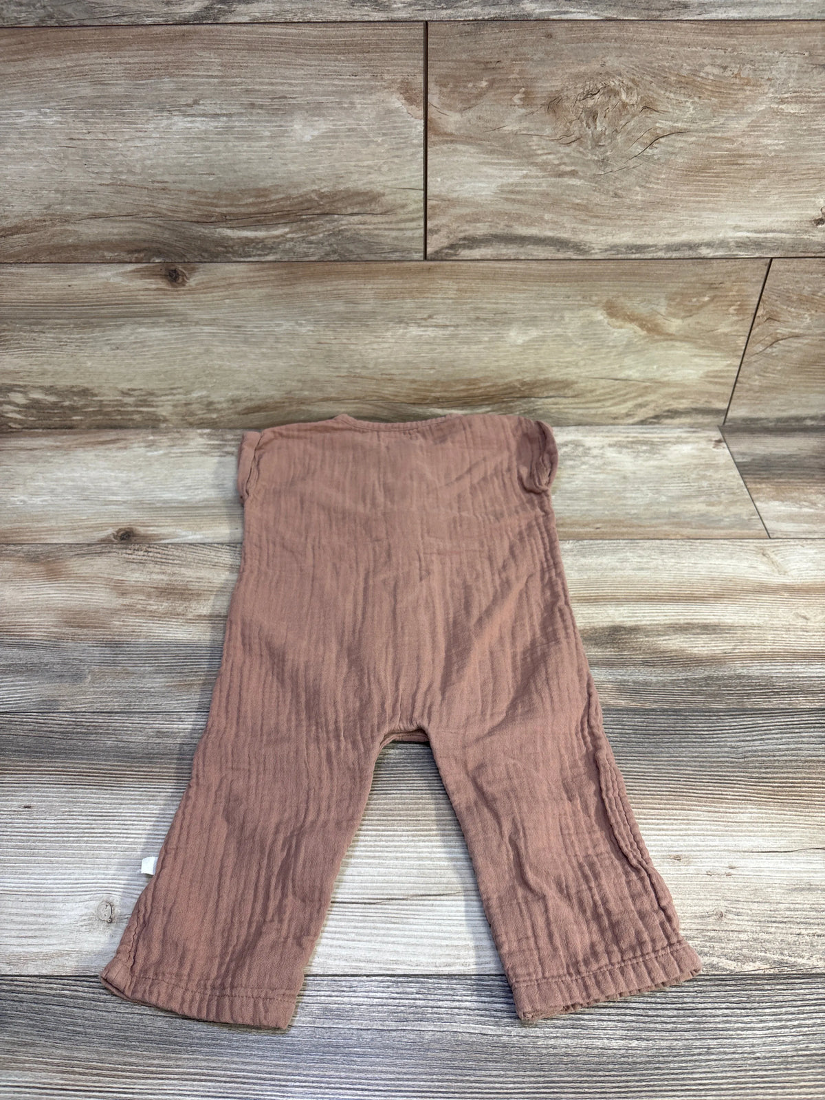 Flat lay of Little Planet organic gauze button-front jumpsuit in brown showing crinkled gauze texture on light wood background