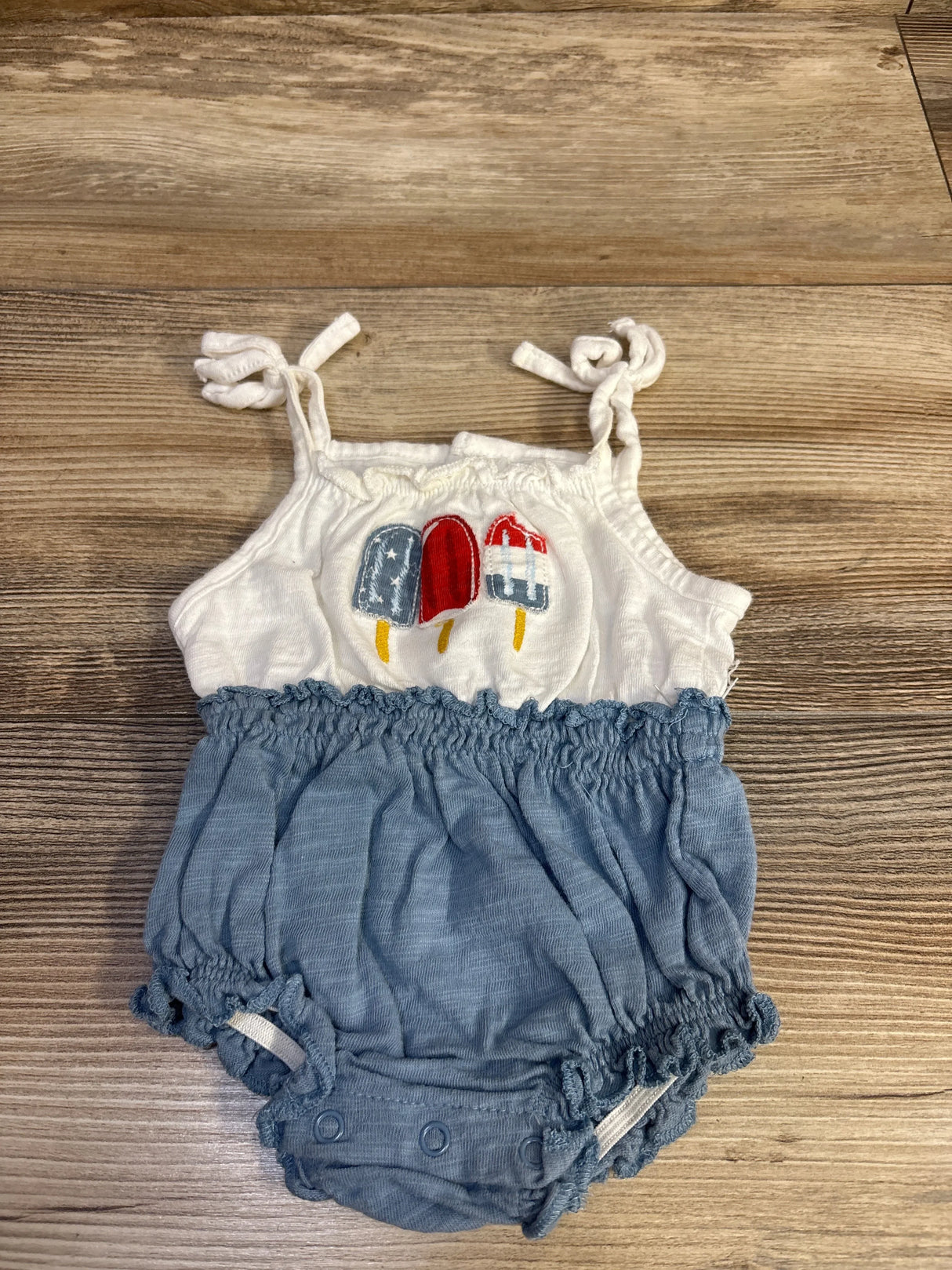 Top view of white and blue baby bubble romper 3M with embroidered patriotic popsicles, knotted shoulder straps and snap crotch