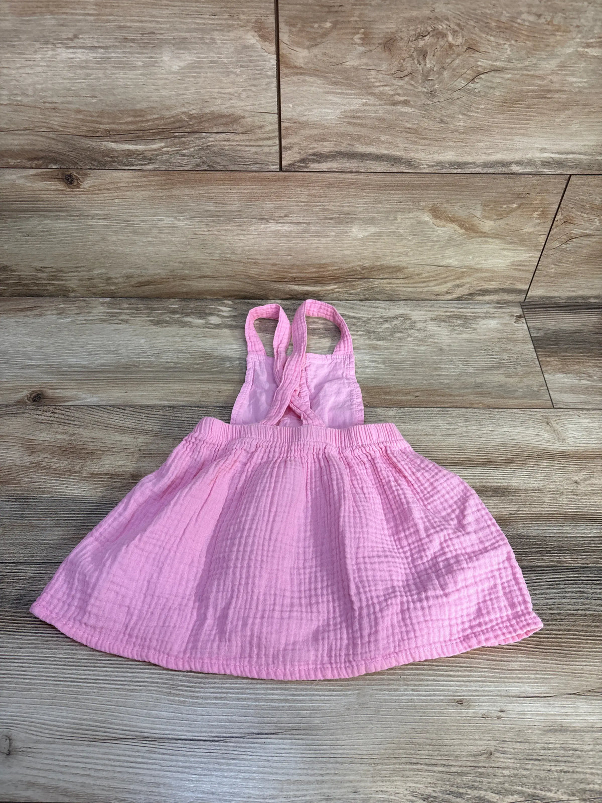 Front view of Young Hearts pink gauze skirtall showcasing crossed shoulder straps and gathered skirt on a wood floor