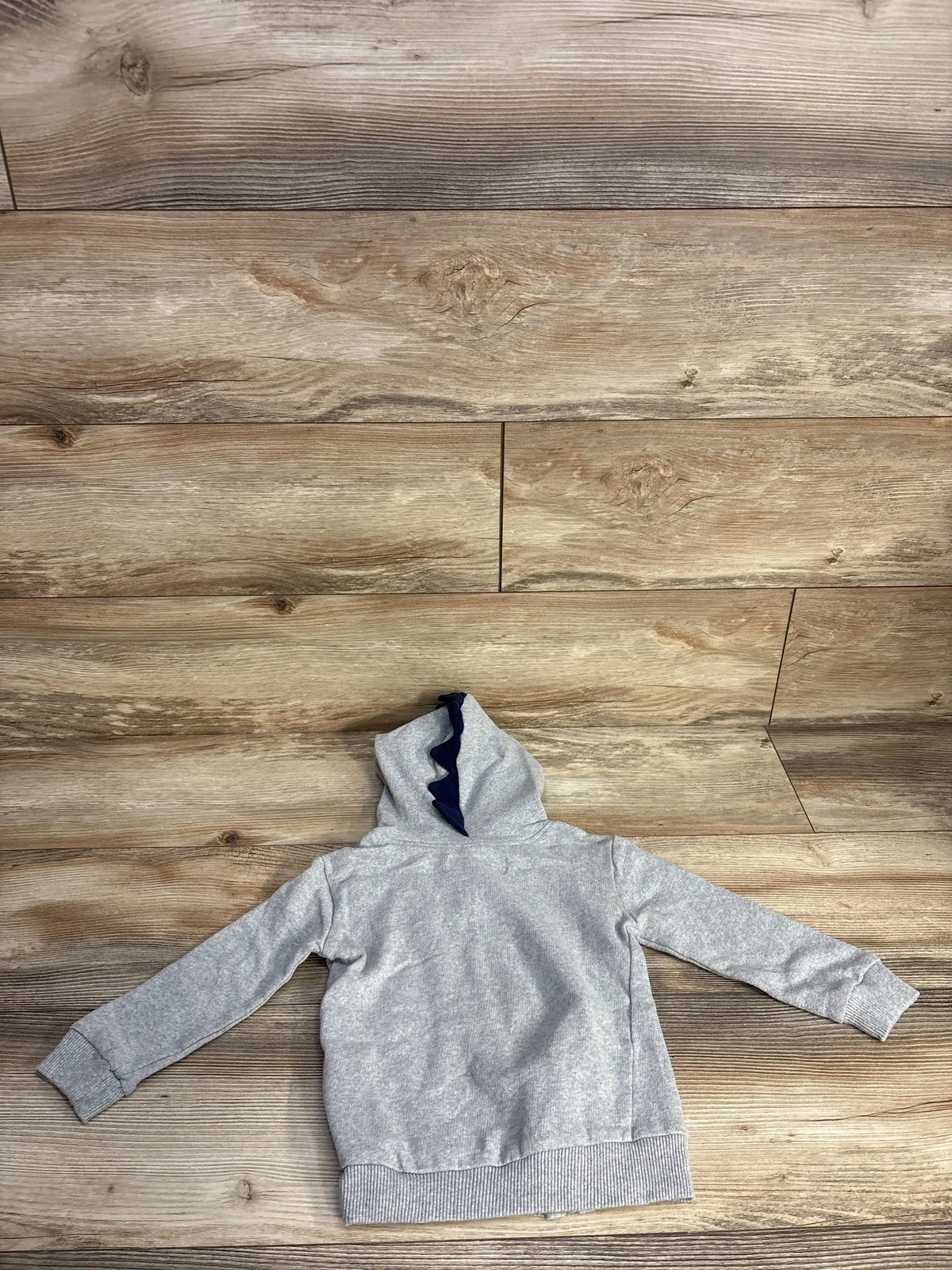 Back view of a gray kids hoodie with navy blue fabric spikes on the hood over wooden floor