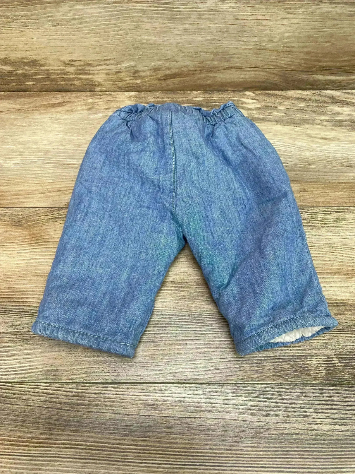Flat front view of Gap chambray baby pants size 0-3M showcasing elastic waistband and sherpa-lined cuffs on wood background