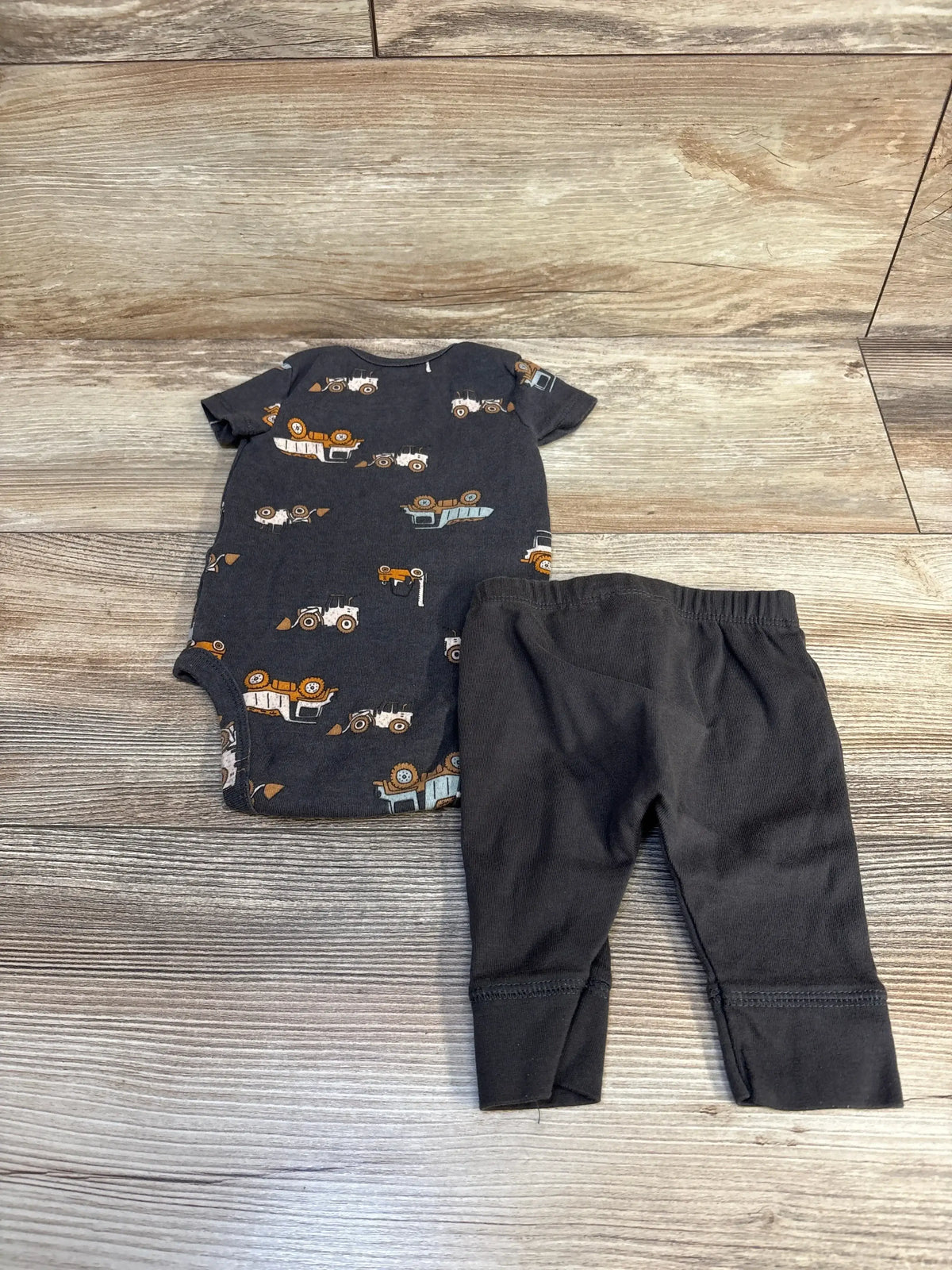 Baby boy outfit with construction vehicle print bodysuit and black pants on wood floor