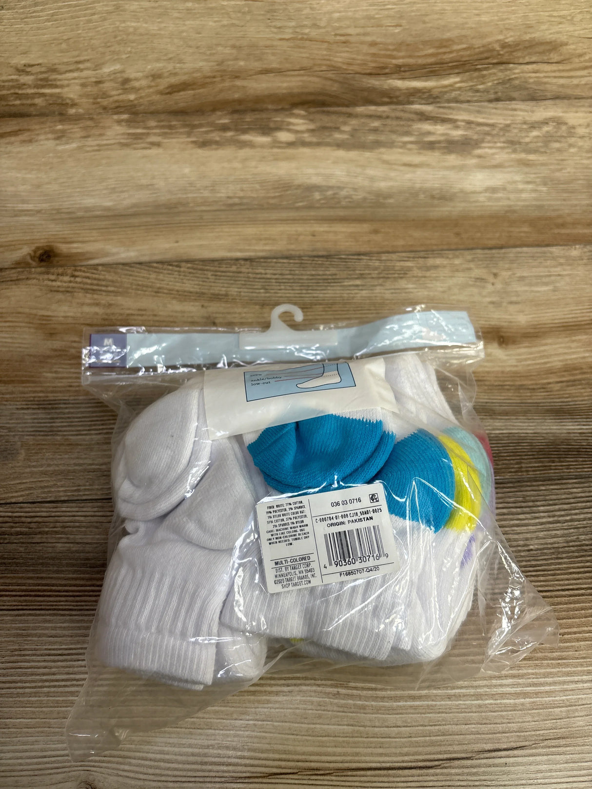 Pack of white crew socks with colorful toe accents in sealed plastic packaging on wood surface