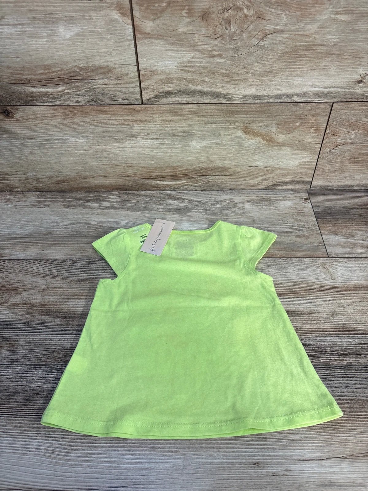 Front view of First Impressions lime shirt showcasing short sleeves and relaxed fit on a wood floor