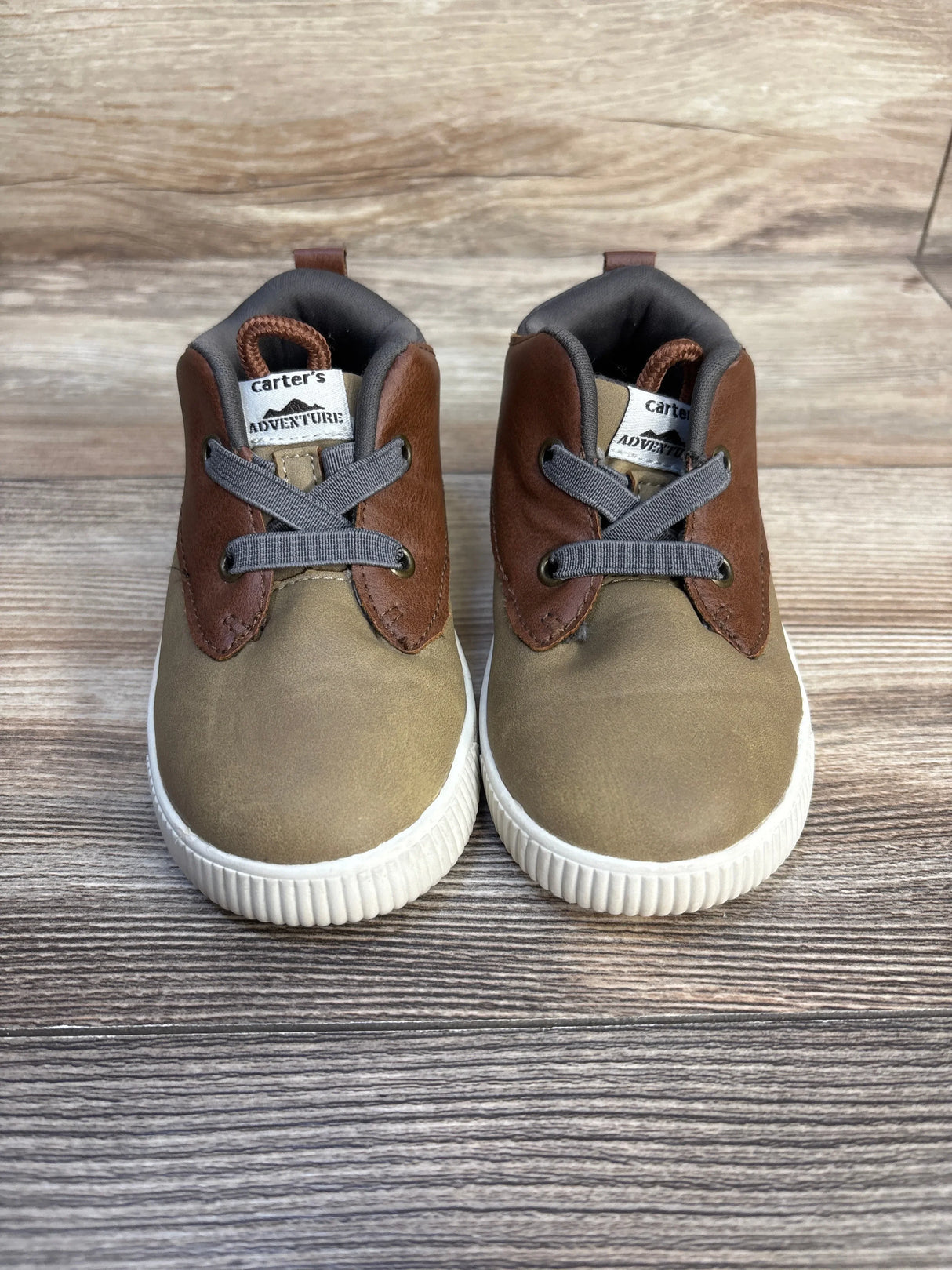 Brown and tan toddler lace-up shoes with white soles on wood background