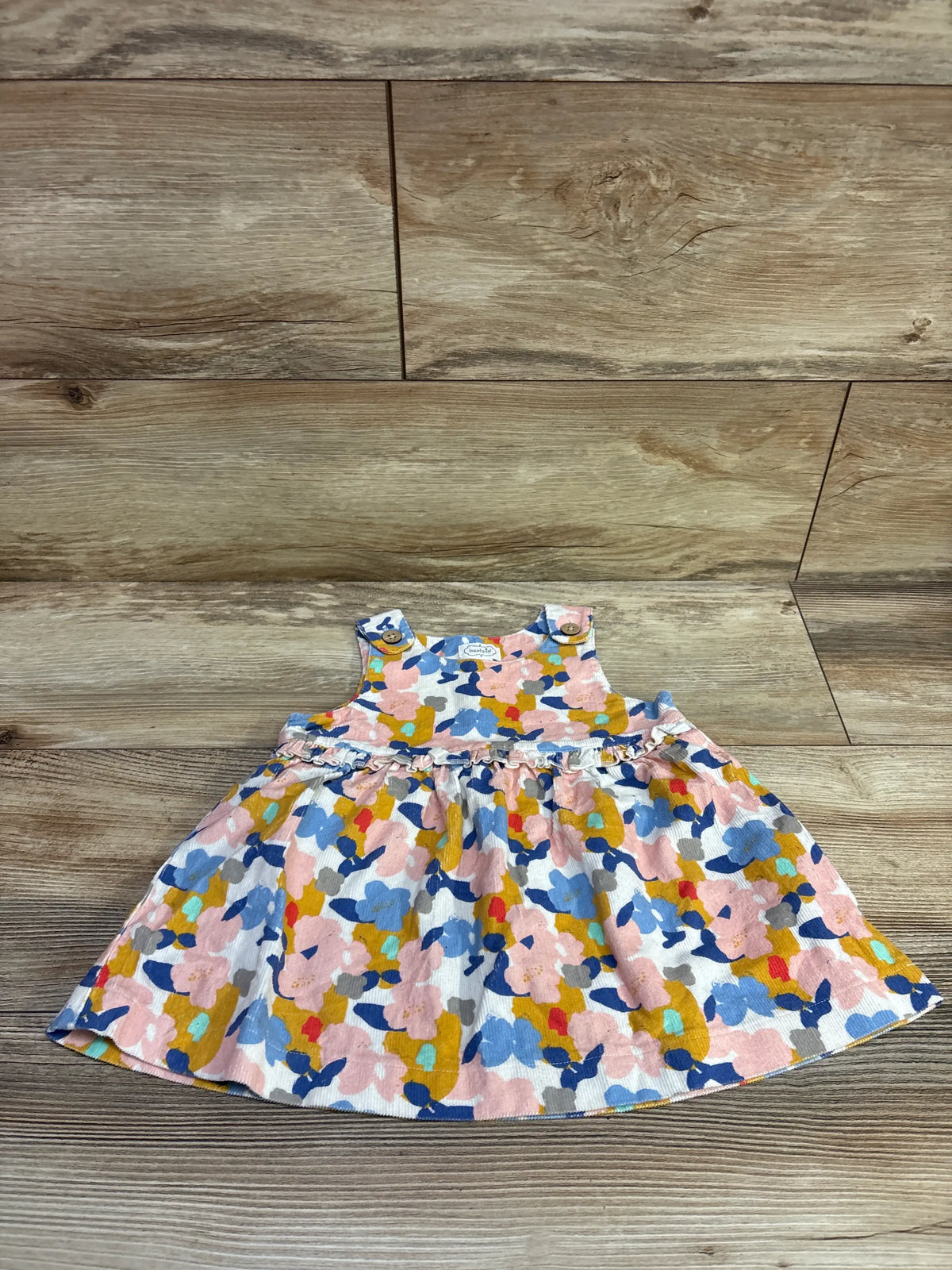 Front view of MudPie floral sleeveless dress in size 9 to 12 months showcasing a ruffled waist and flared skirt on a wood floor