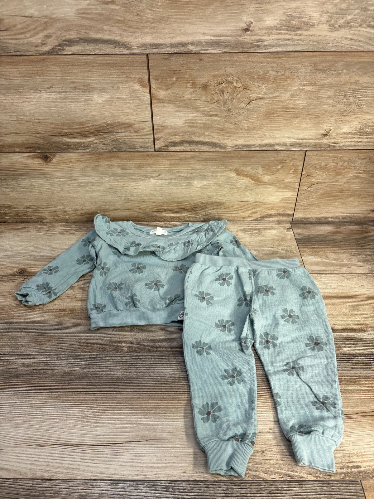 Flat lay of green Rabbit + Bear 2pc sweatshirt and pants set with ruffle collar and floral print on wood background