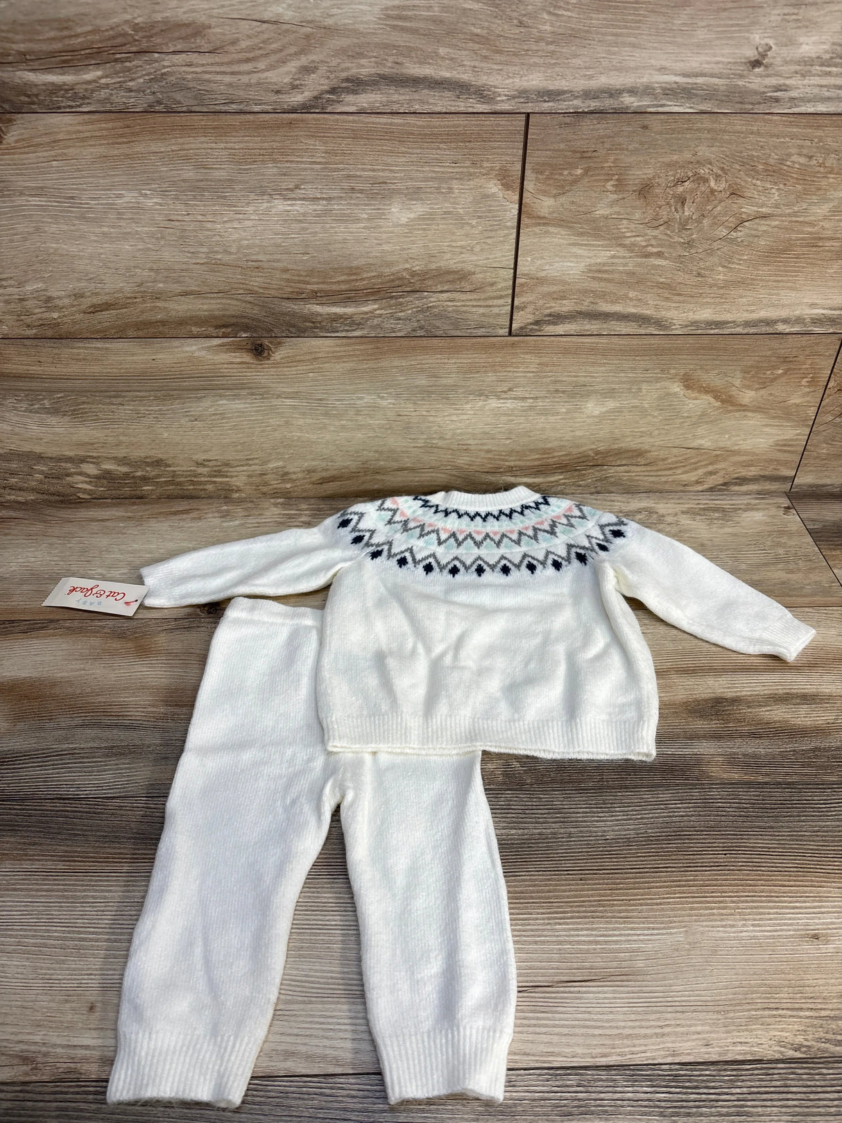 White knit baby sweater and pants set with geometric pattern, laid on wooden floor