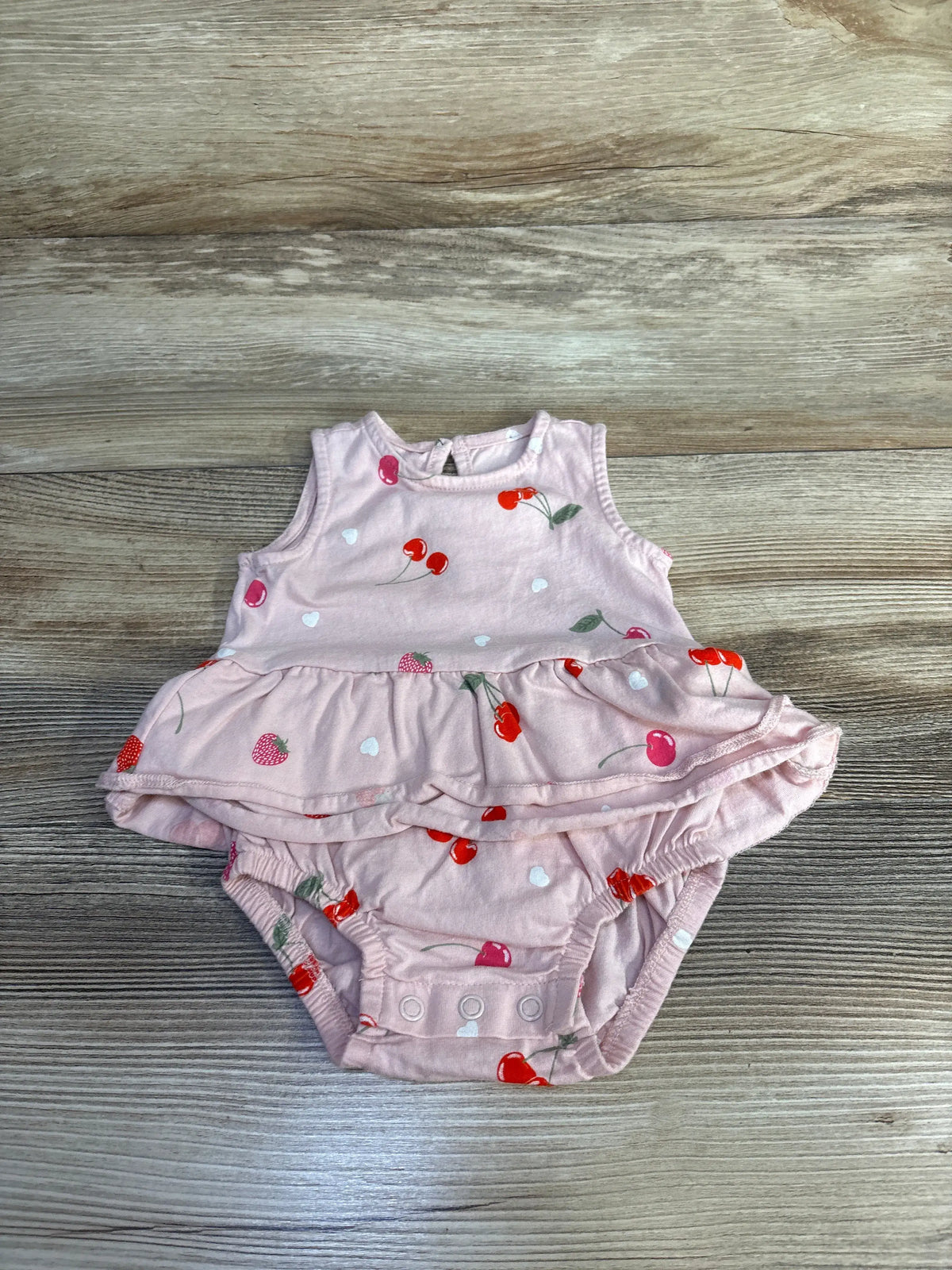 Front view of Carter’s pink cherry bodysuit dress showcasing ruffled skirt and snap closures on a wood background