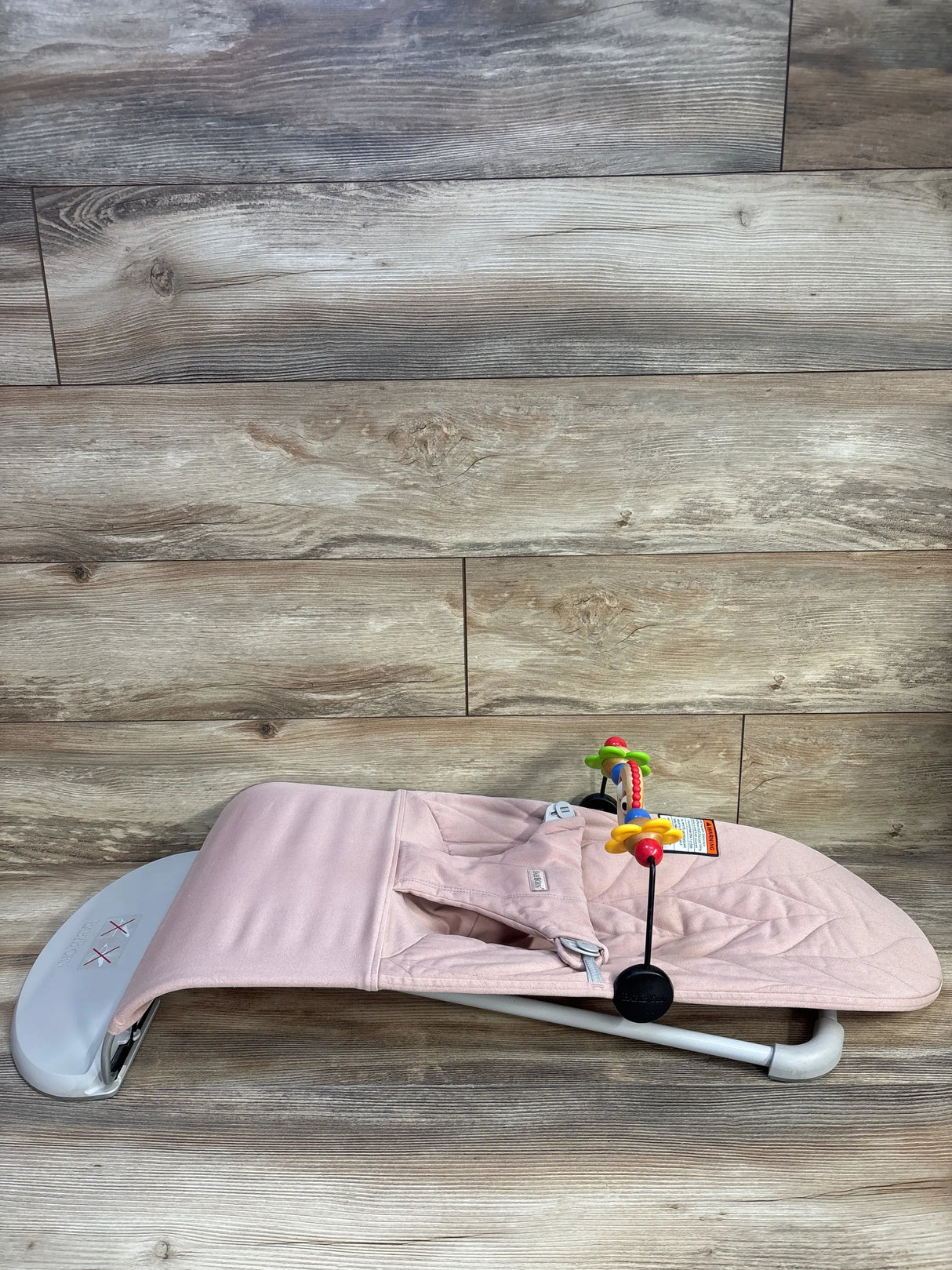 Side view of Baby Bjorn Bouncer Bliss in dusty pink showing quilted petal seat and attached toy bar on wood floor