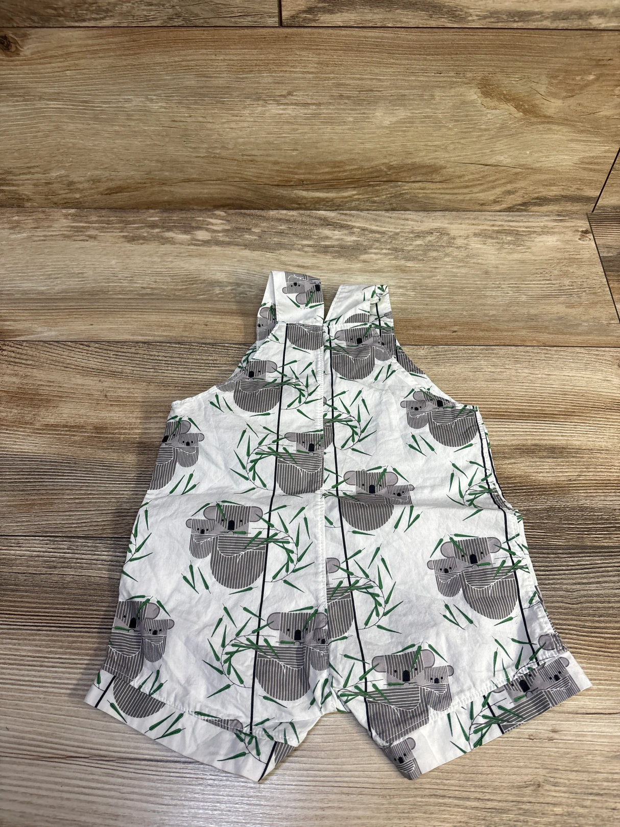 Flat lay of Little Stitches Koala Taylor shortalls showing front koala print and green bamboo motifs on wood floor background