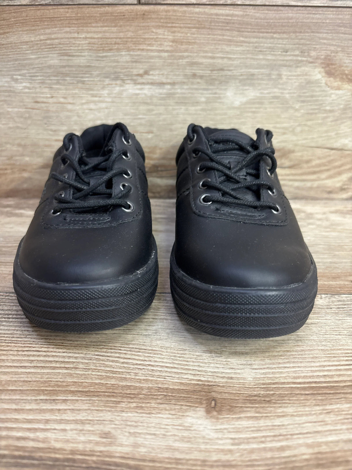Pair of black lace-up kids sneakers on wood background, gently used children’s shoes