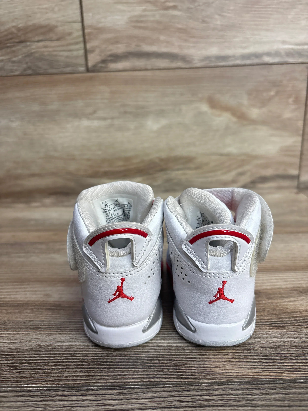 Pair of white and red toddler Air Jordan sneakers on wooden floor, kids' footwear resale