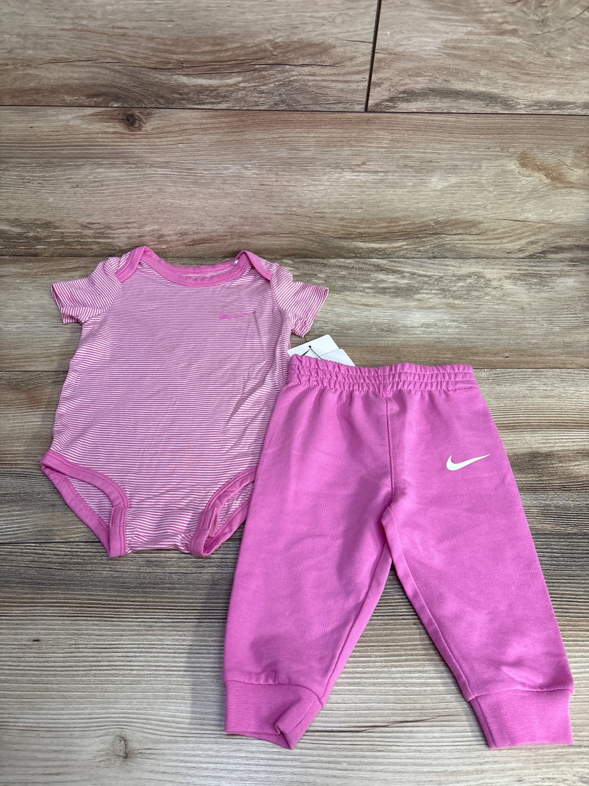 Pink striped baby onesie and pink Nike sweatpants set on wooden background