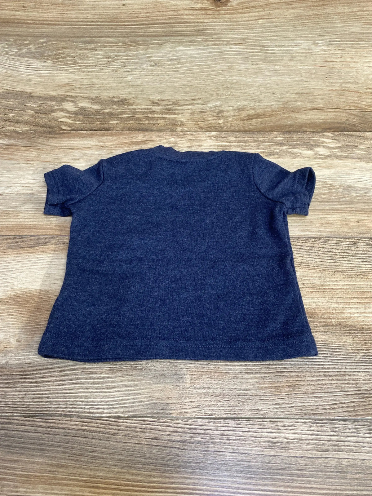 Back view of newborn navy Tommy Hilfiger short-sleeve baby shirt showing plain back and crew neckline on wooden surface
