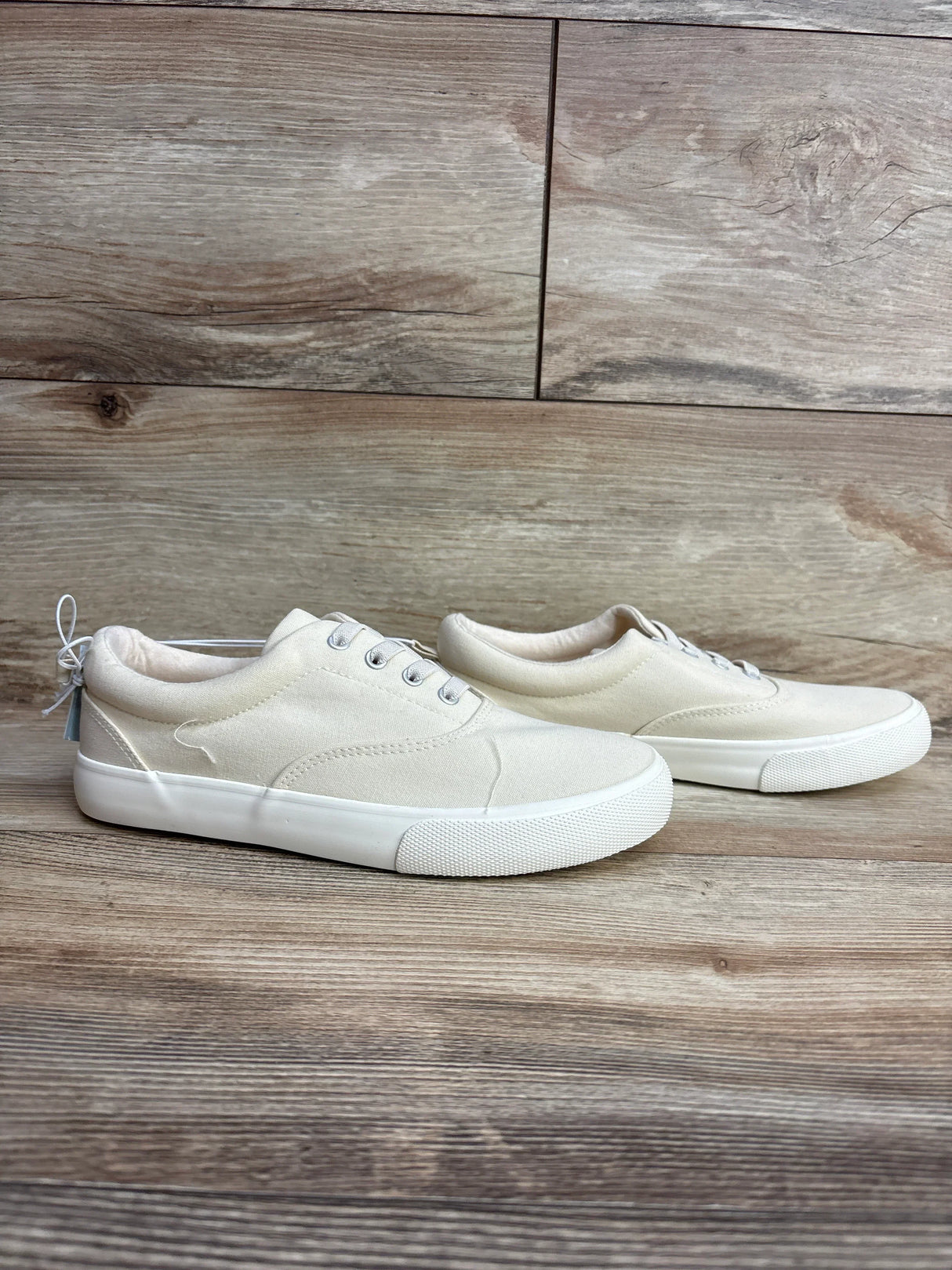 Pair of kids' off-white canvas sneakers with rubber soles on a wooden floor