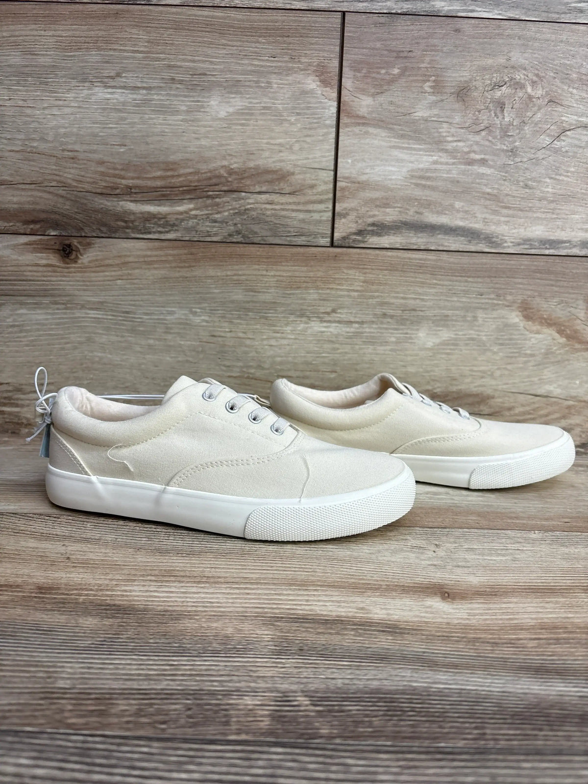 Pair of kids' off-white canvas sneakers with rubber soles on a wooden floor