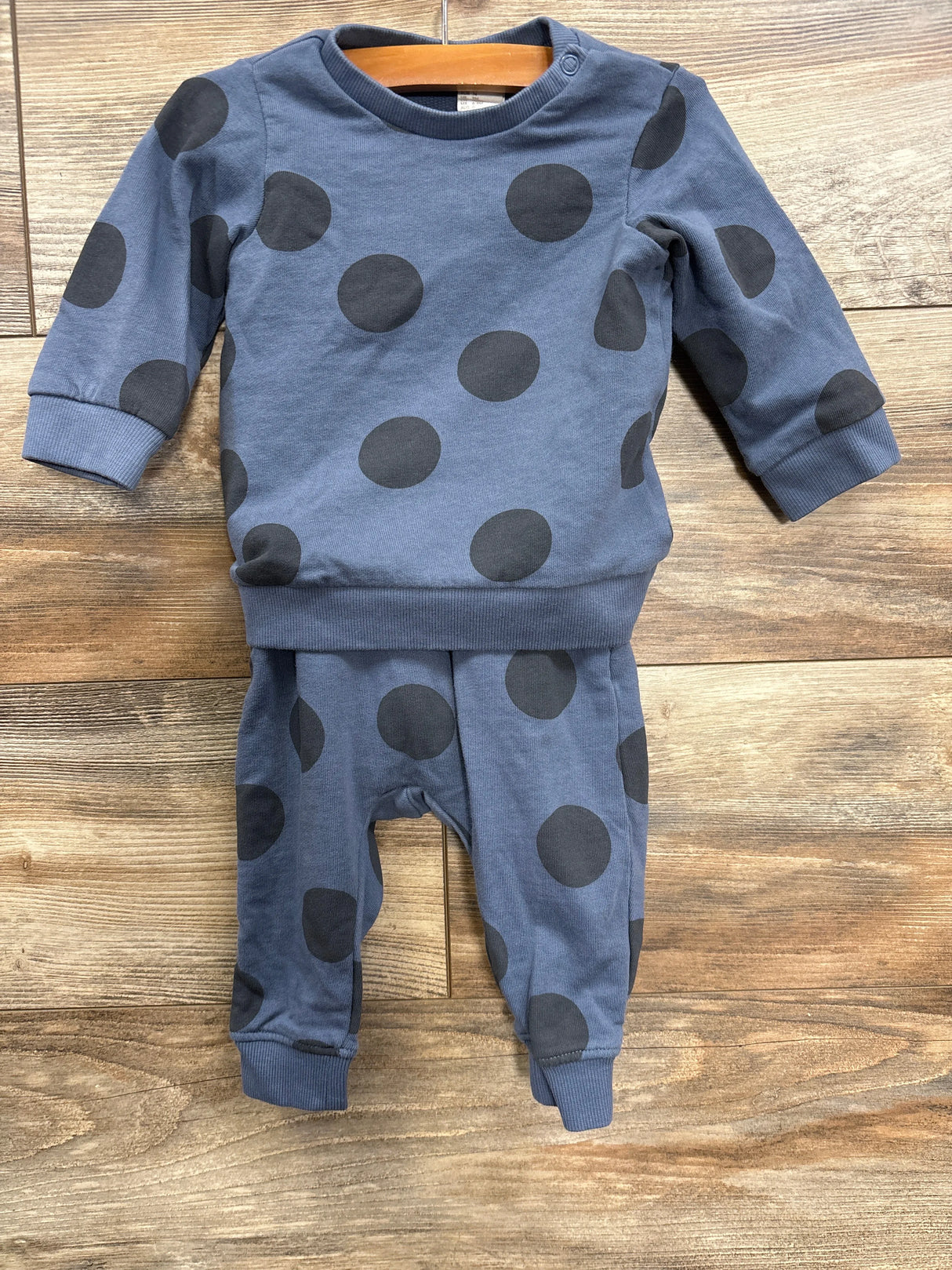 Blue baby outfit with black polka dots, long sleeve top and pants on wooden floor