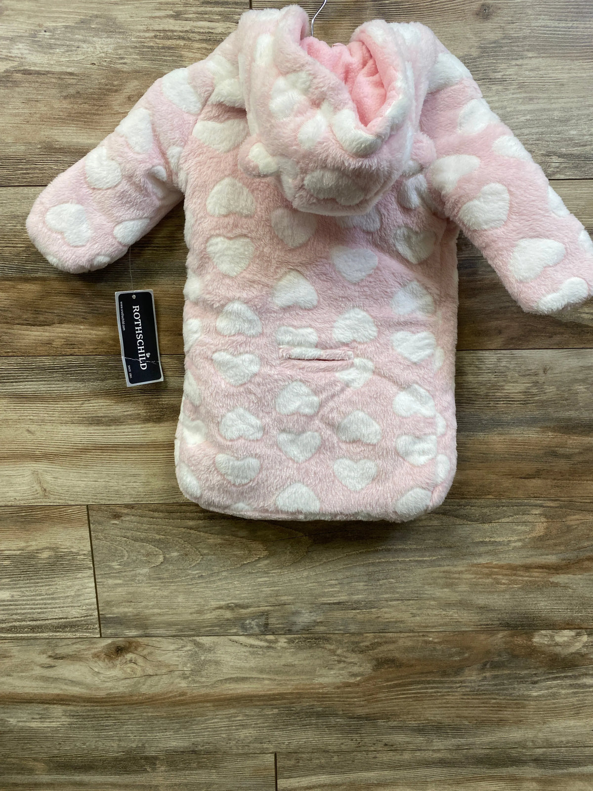 Front view of pink Rothschild faux fur hooded car bag for size 0/6 months with white hearts on a wood background