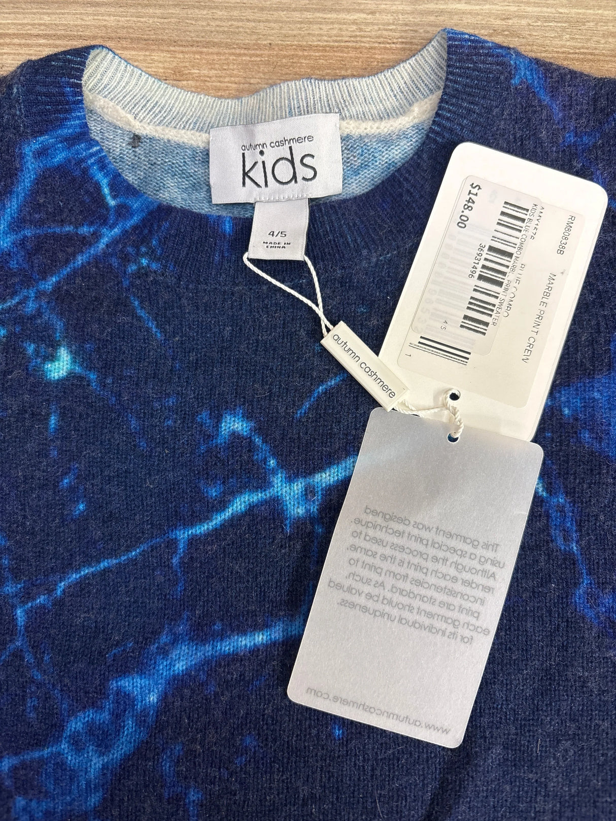 Top down close up of Autumn Cashmere kids crew sweater showing blue marble print and 4/5 size tag on wooden floor